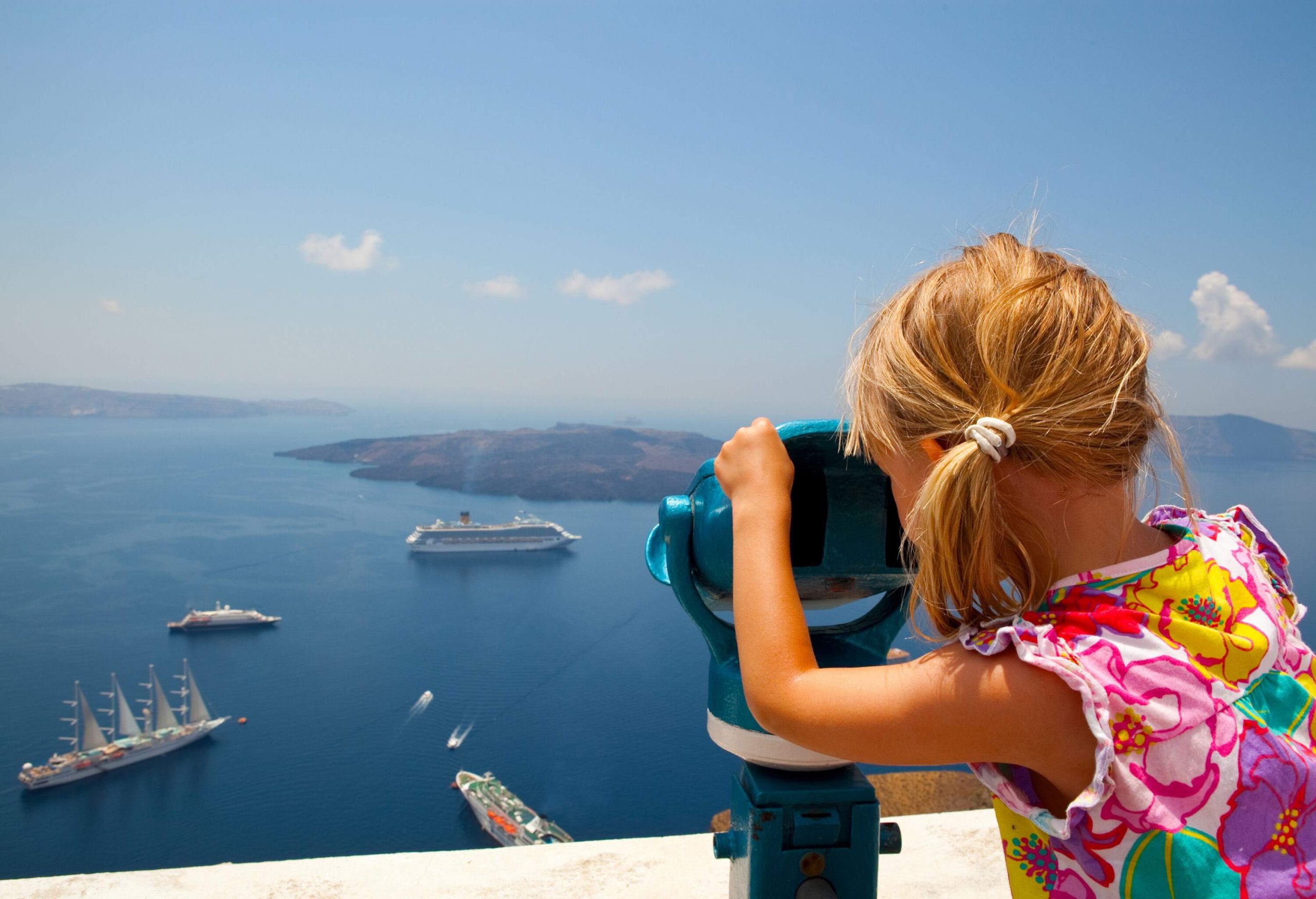 A little girl looking through binoculars at the boats cruising in the ocean from an observation deck.