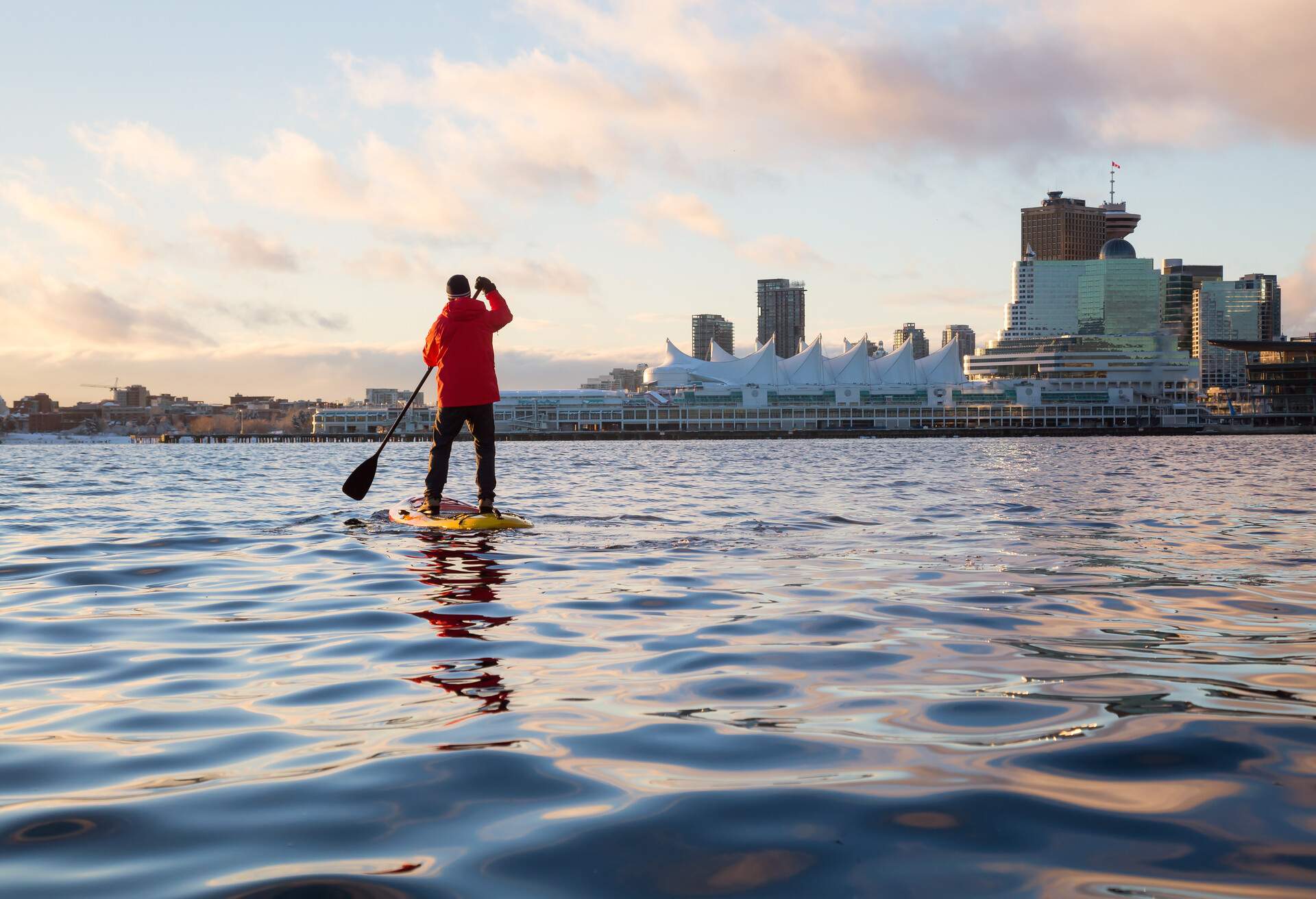 A man paddleboarding in the Burrard Inlet with the Canada Place in the background.