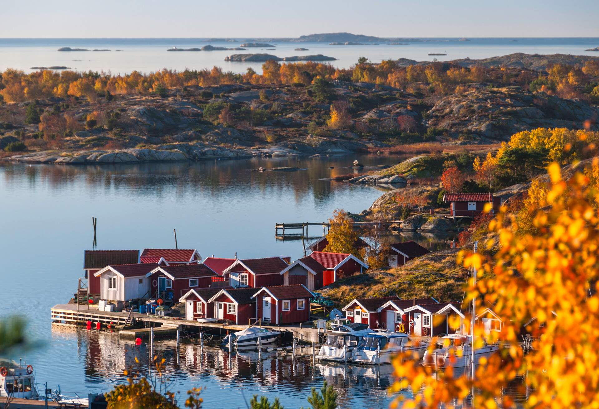 Tiny maroon cottages on an extended wooden platform alongside docked boats lie on a coastal village.