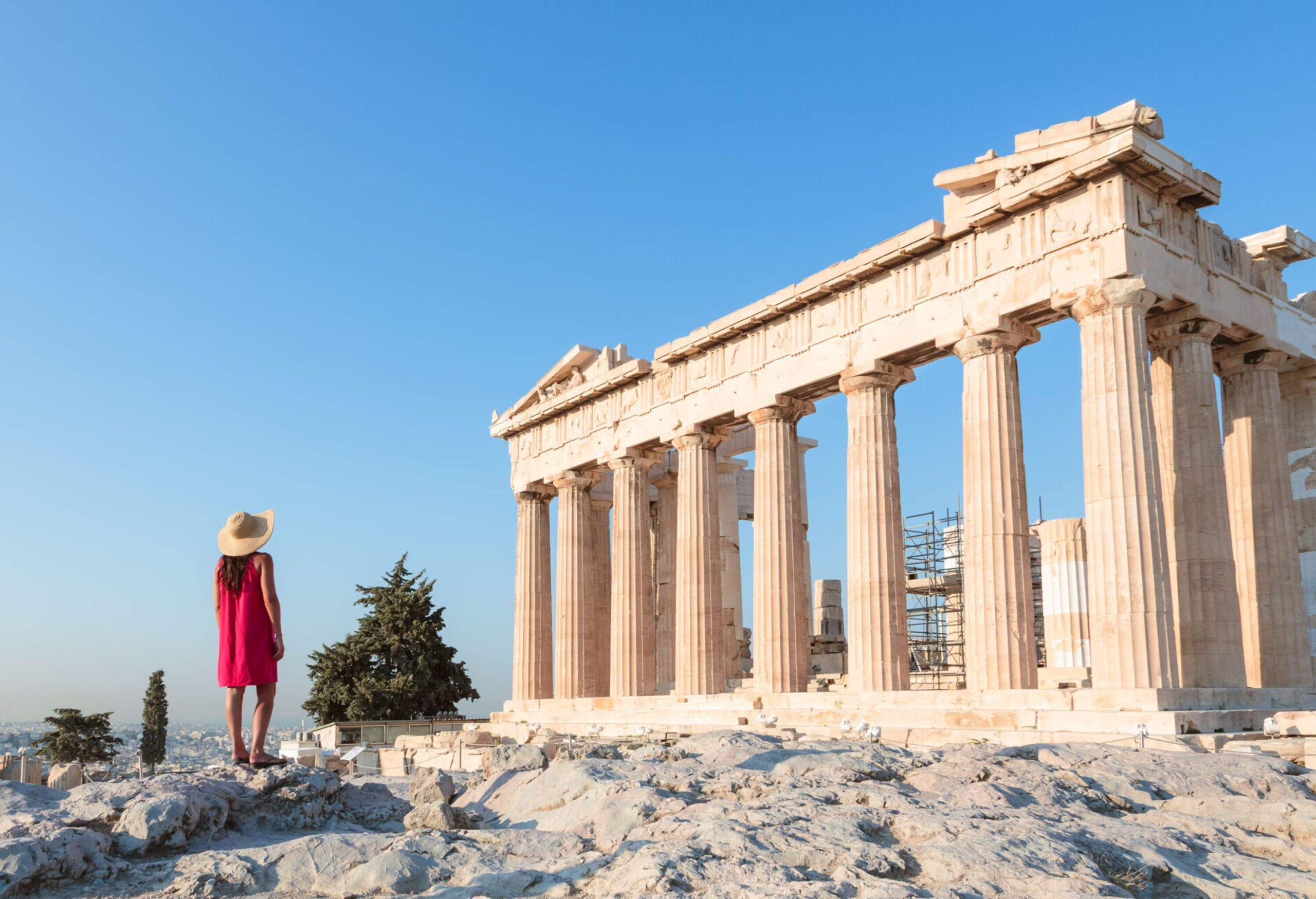 A woman in a pink dress is standing in front Parthenon temple on the Acropolis, Athens, Greece.