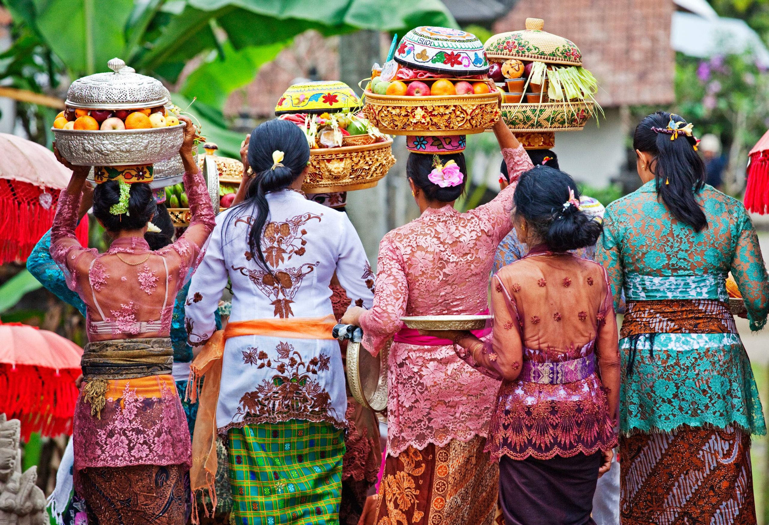Women in colourful traditional lace clothing walk with others carrying fruit baskets on their heads.