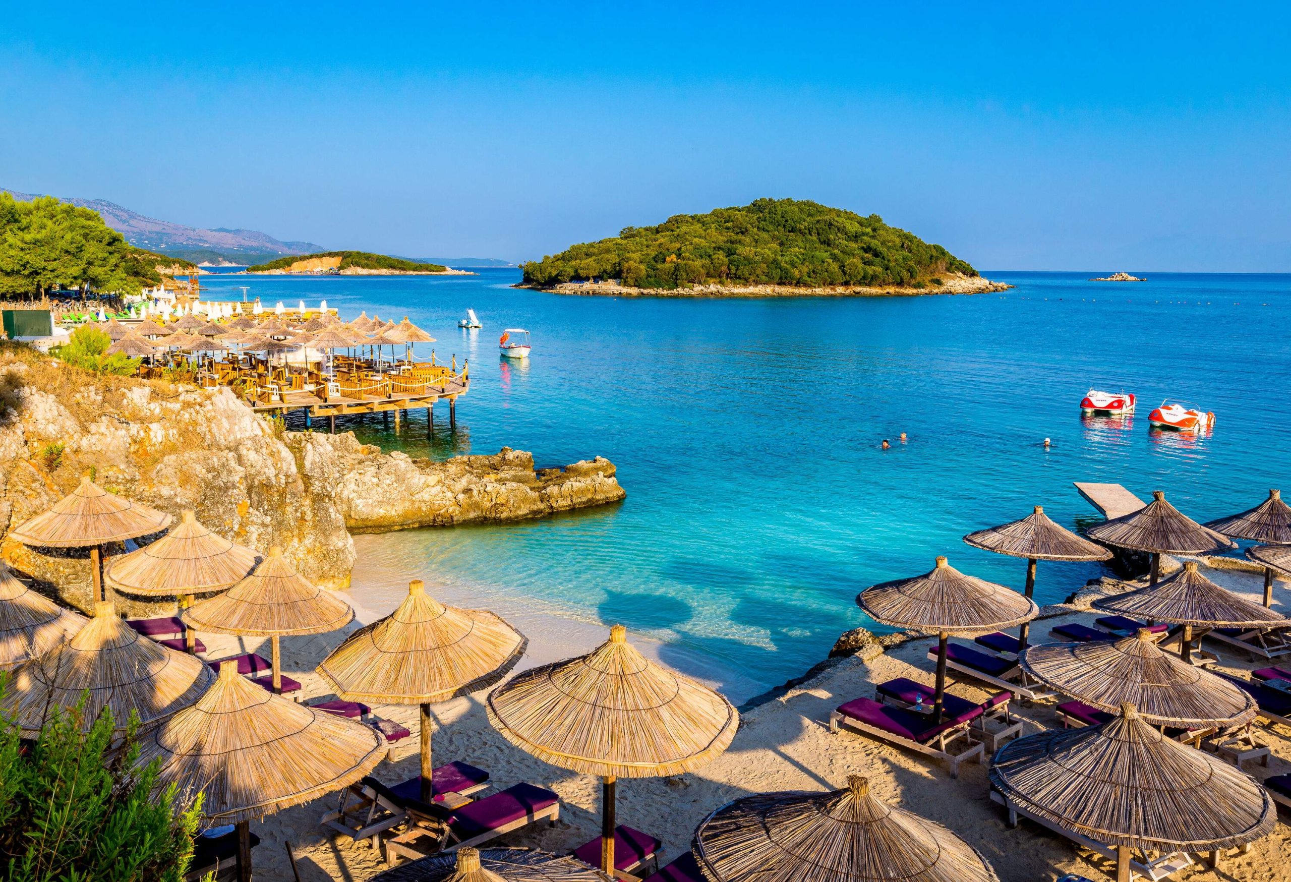 Picturesque view of a luxury beach resort with thatch umbrellas, deckchairs and boats.