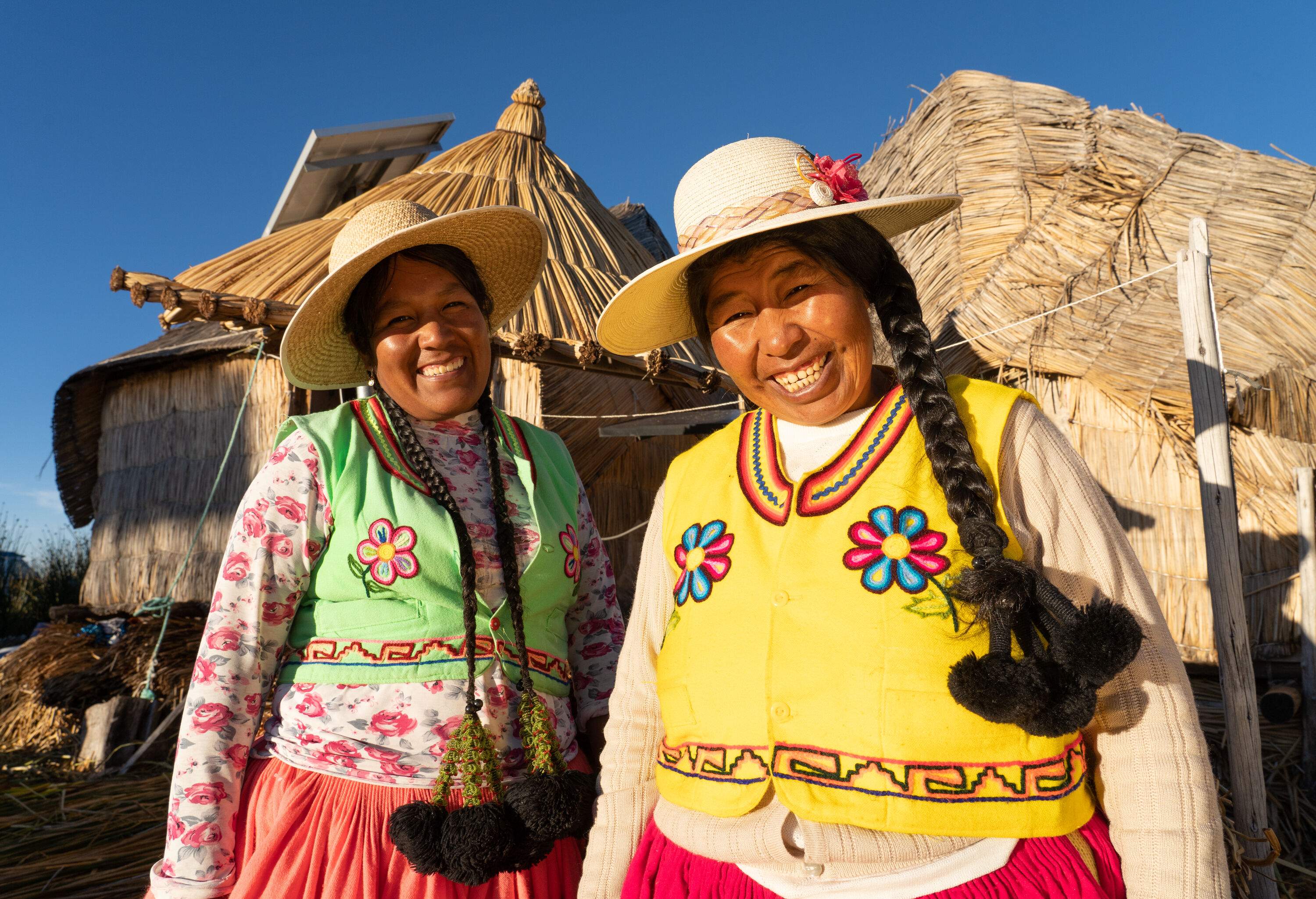 Two peruvian indigenous women smiling at the camera wearing traditional clothes