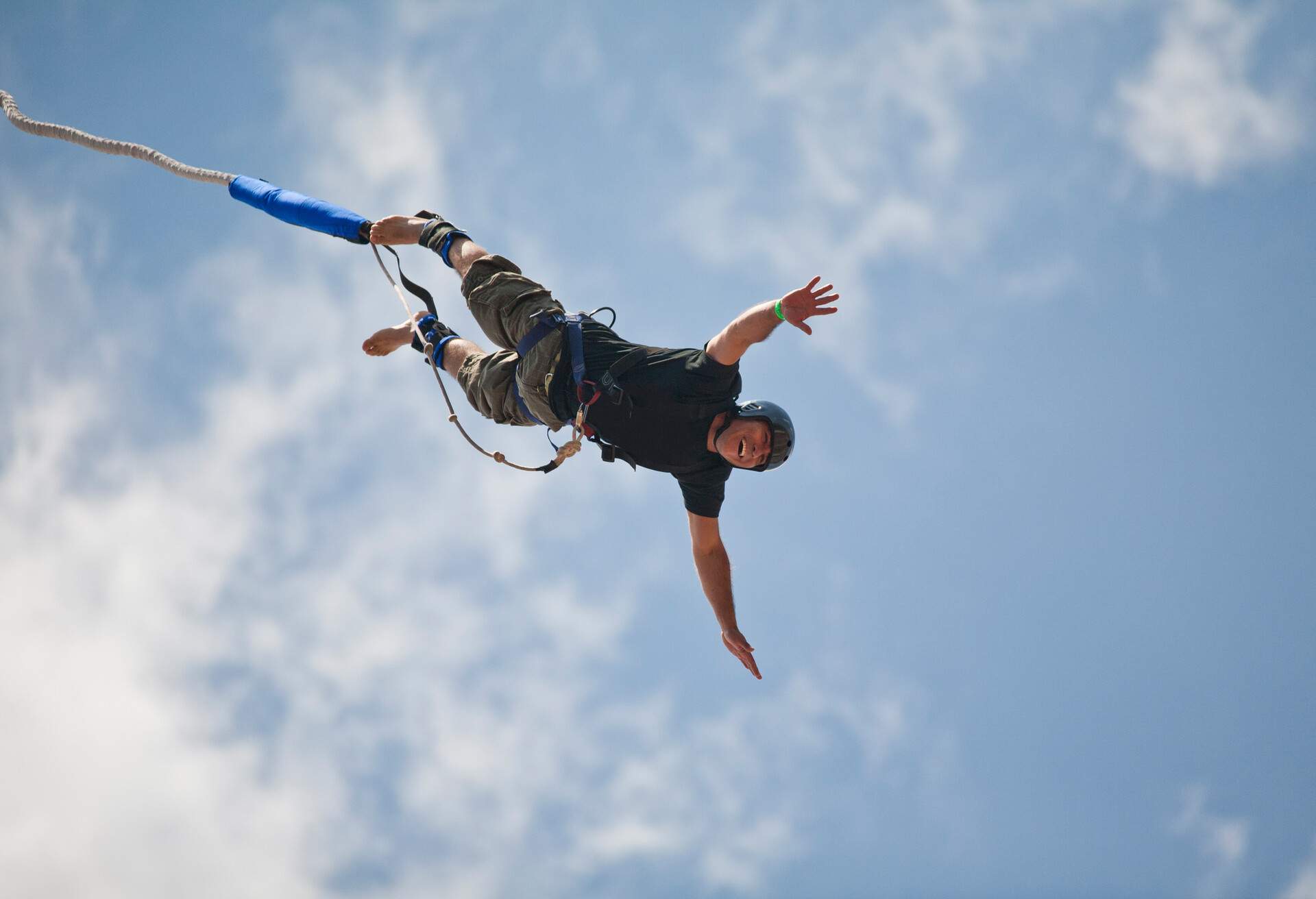 A man in a helmet bungee jumps while attached to a rope.
