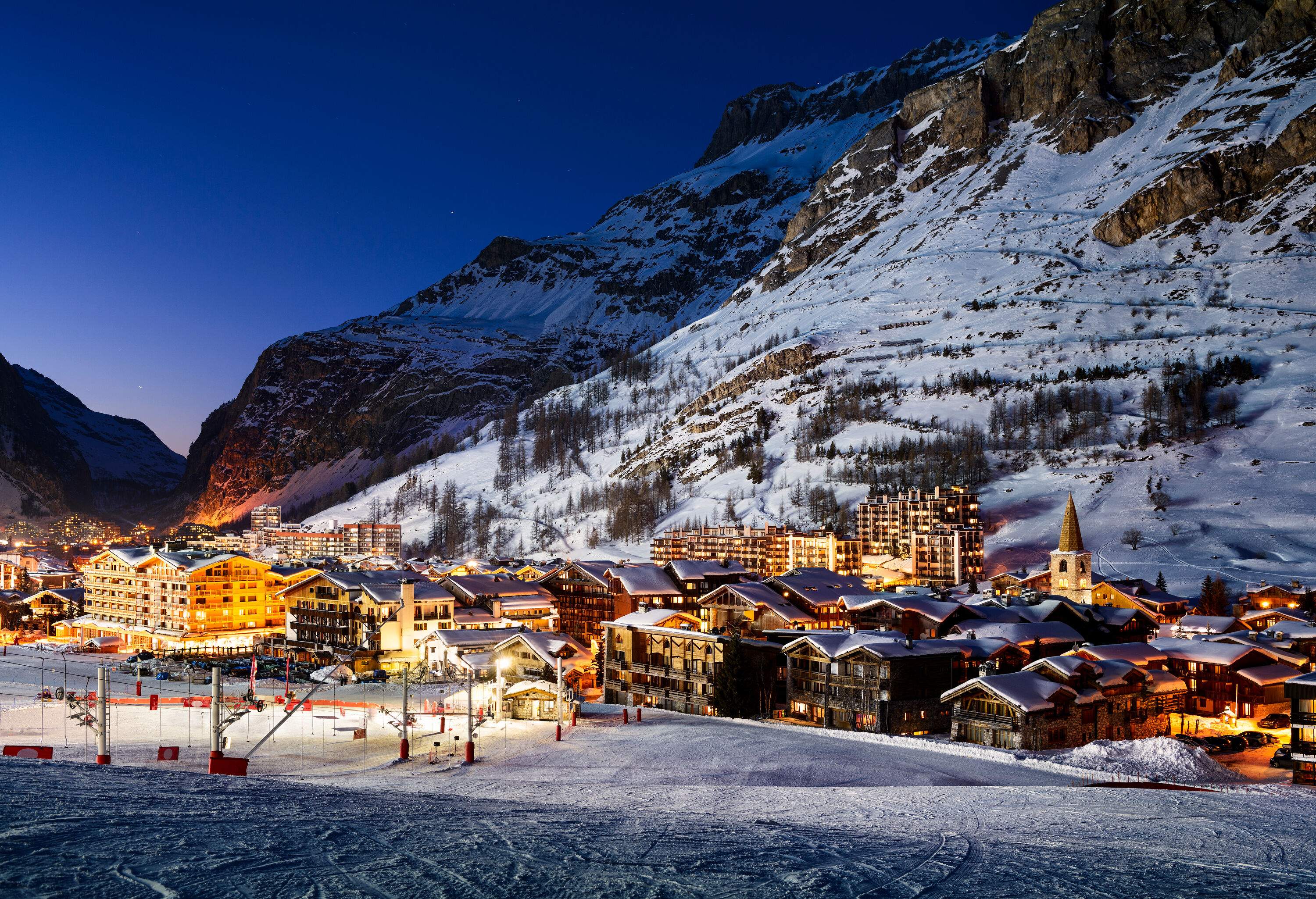 A picturesque snow-covered hillside community with bright lights and gondolas.