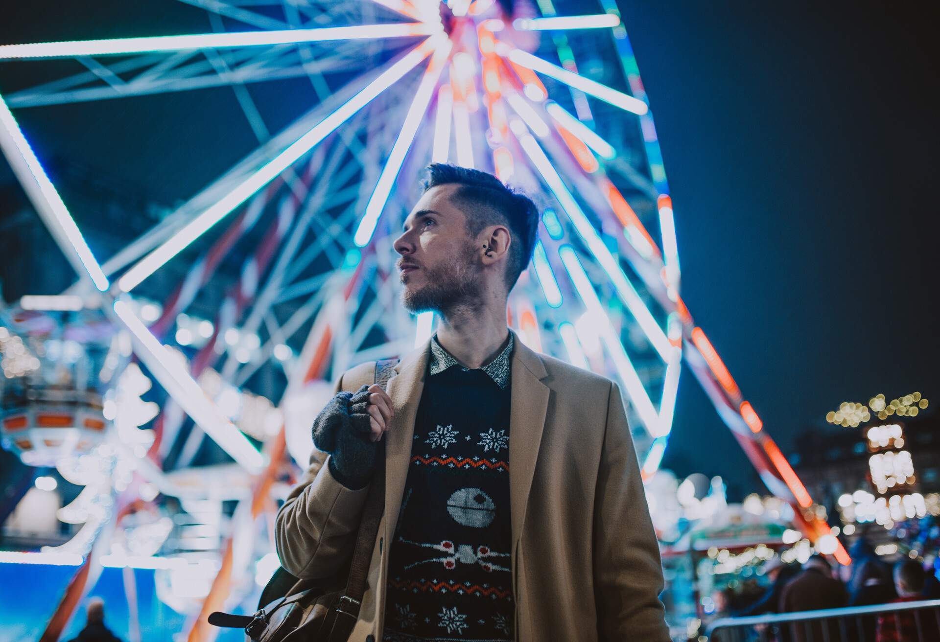 Un homme en vêtements chauds se tient devant une grande roue aux lumières vives.