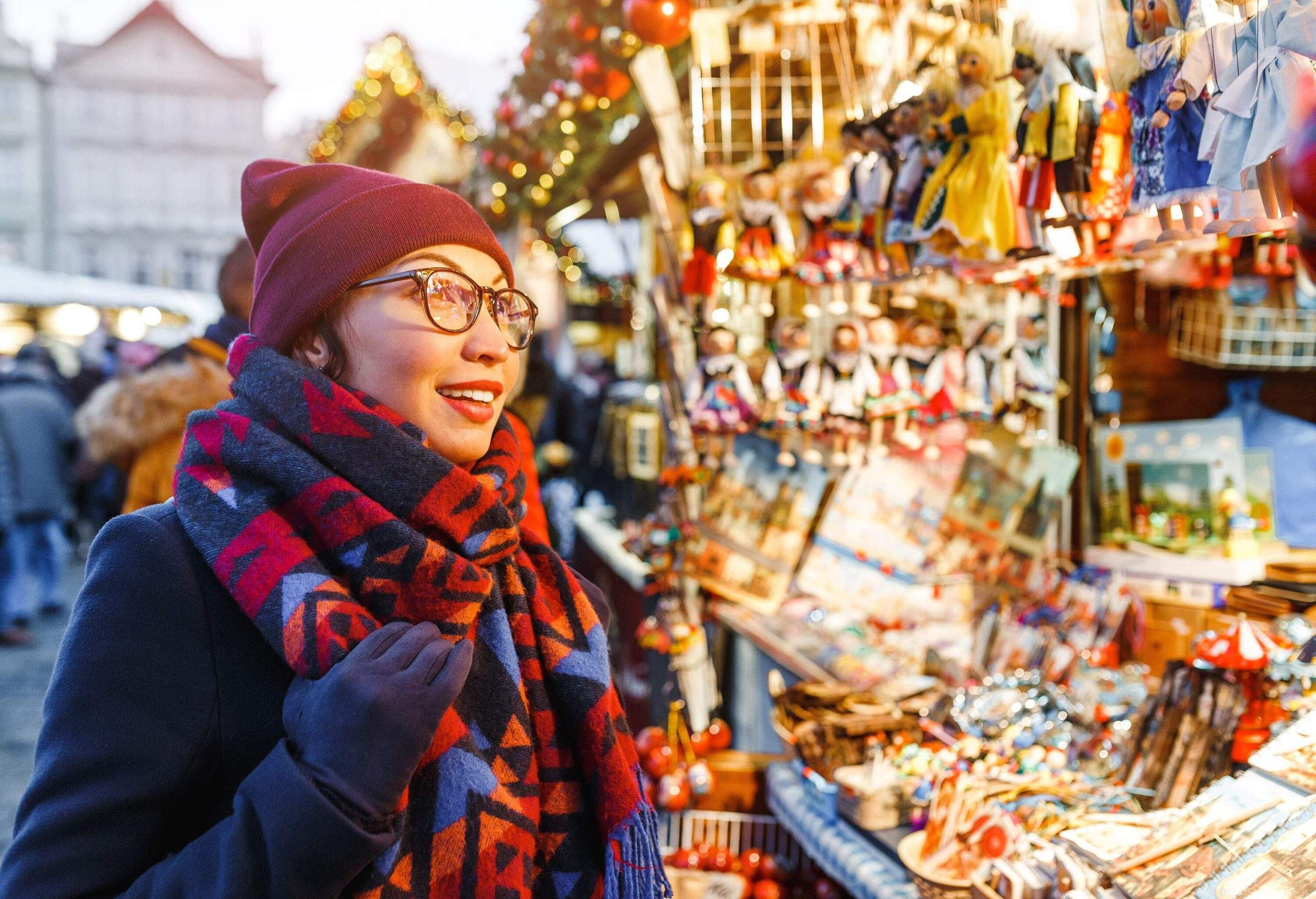Femme joyeuse en vêtements chauds et écharpe admirant la variété de souvenirs de Noël colorés en vente.