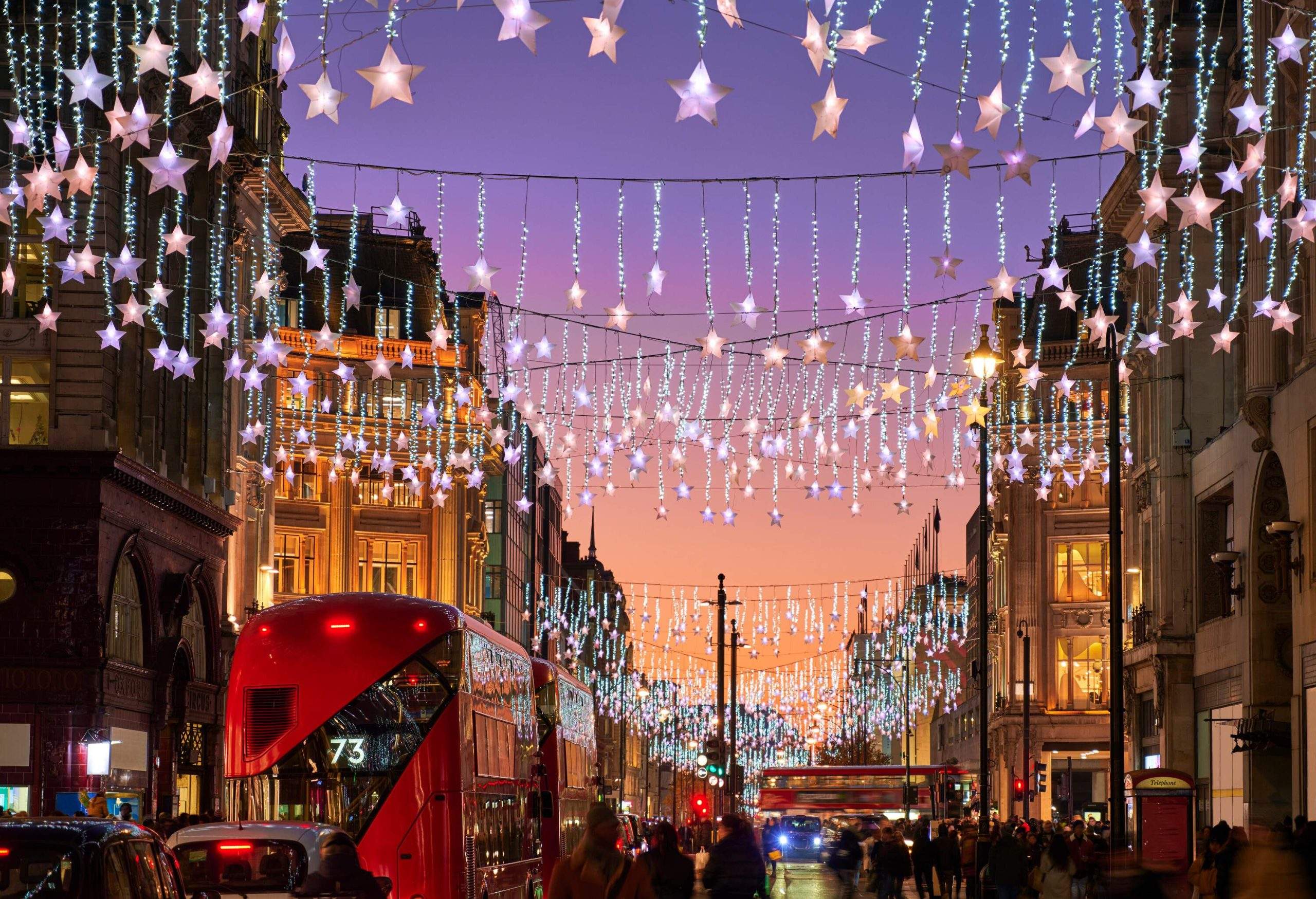 Des guirlandes lumineuses de Noël suspendues au centre d’une rue commerçante pleine de monde.