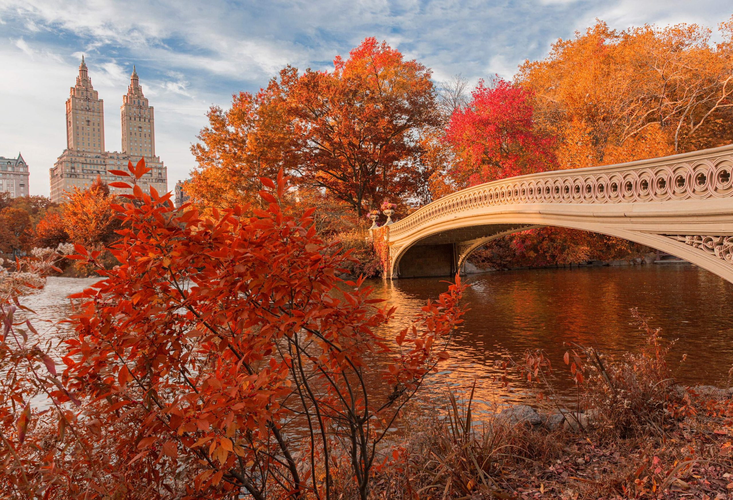 In front of a majestic structure with twin towers, the bow bridge crosses a lake surrounded by lush vegetation.