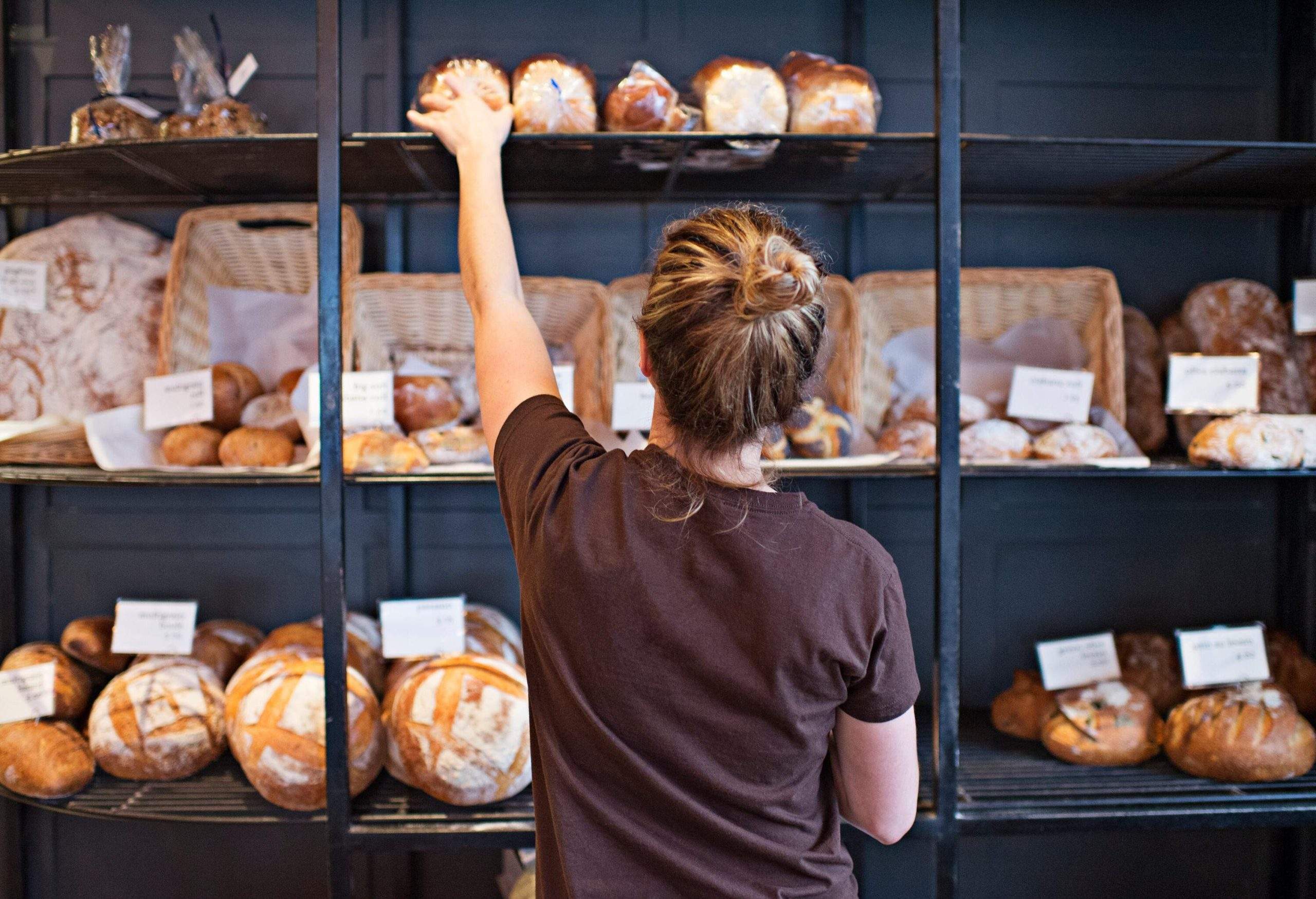 Une femme remplit les étagères avec des miches de pain fraîchement cuites.