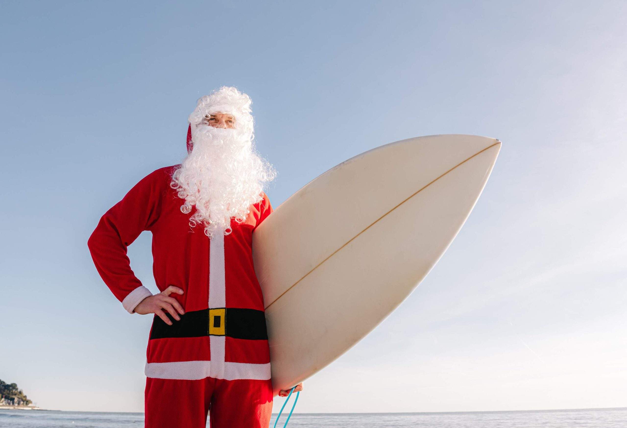 Un homme déguisé en Père Noël avec une planche de surf sous le bras