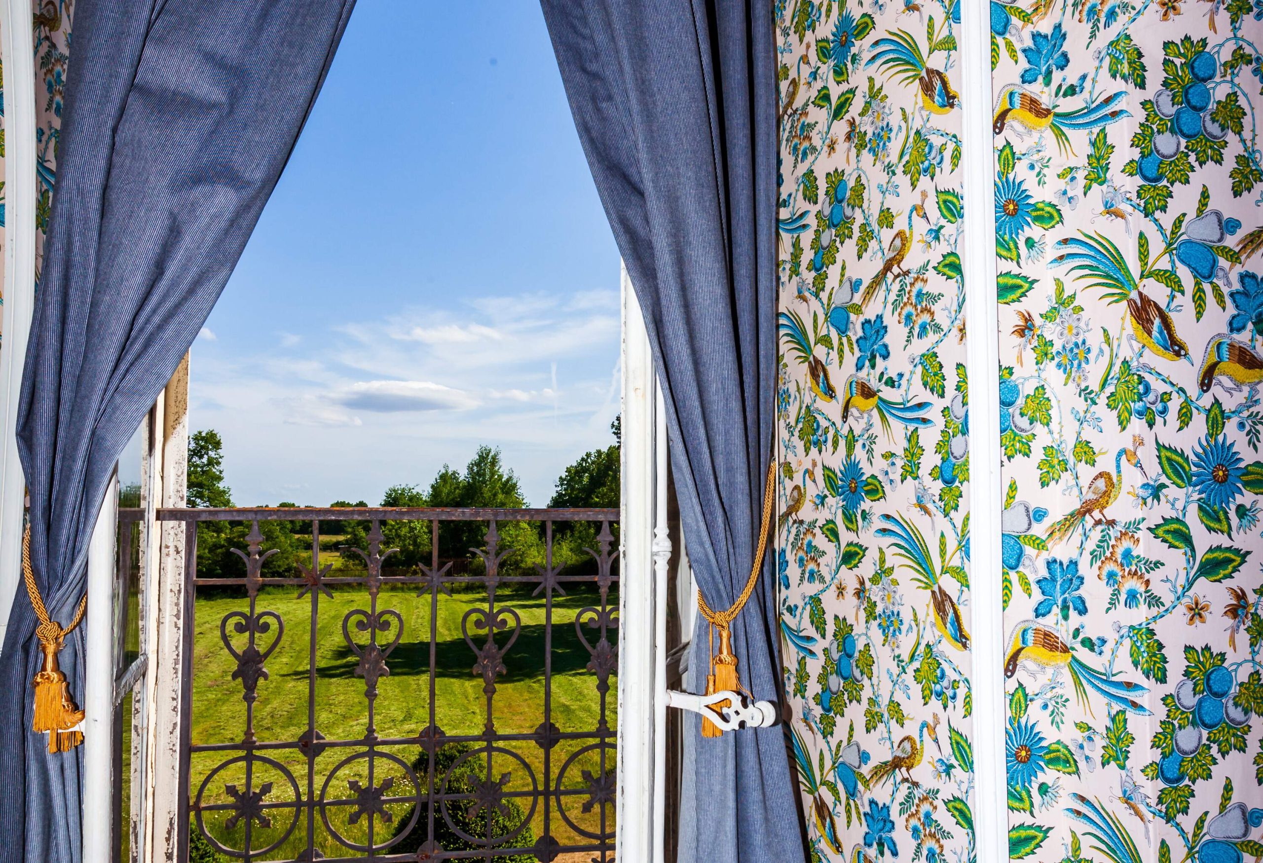 An open balcony door designed with a blue curtain and a view of a lush green lawn. 