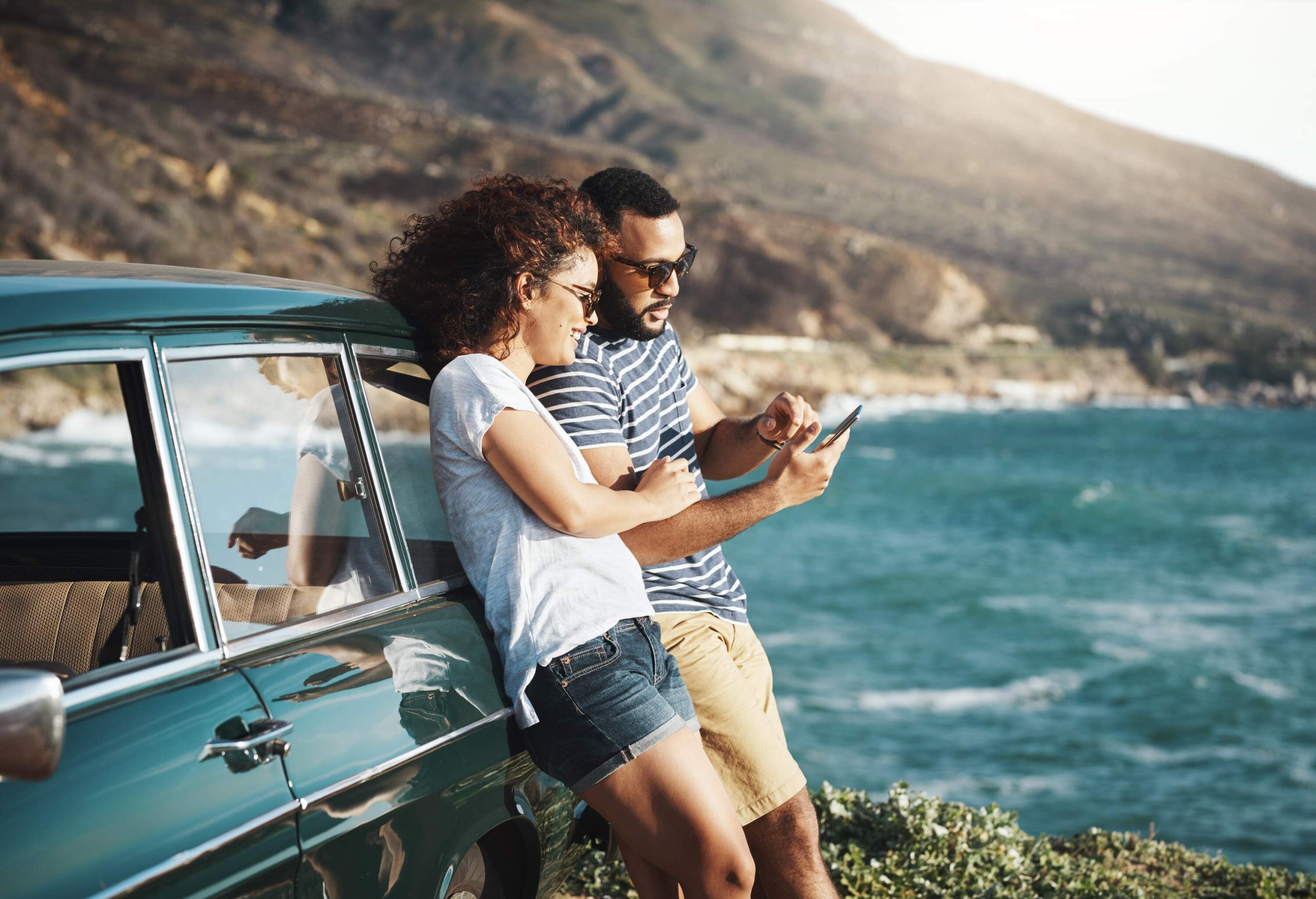 Two people standing next to a car and looking at a smartphone