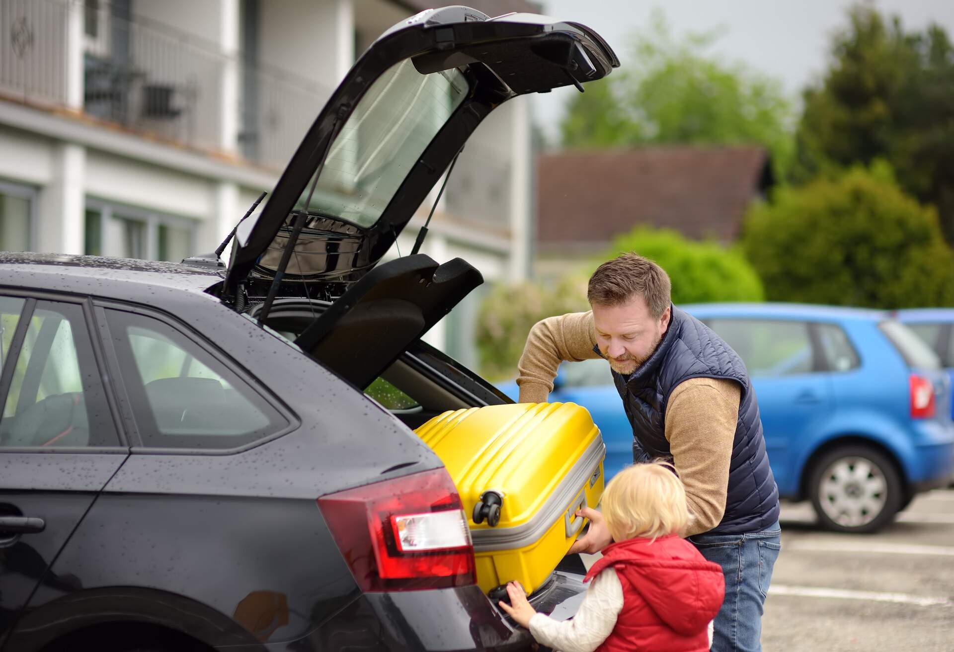A man and a child putting a suitcase in the trunk of a rental car