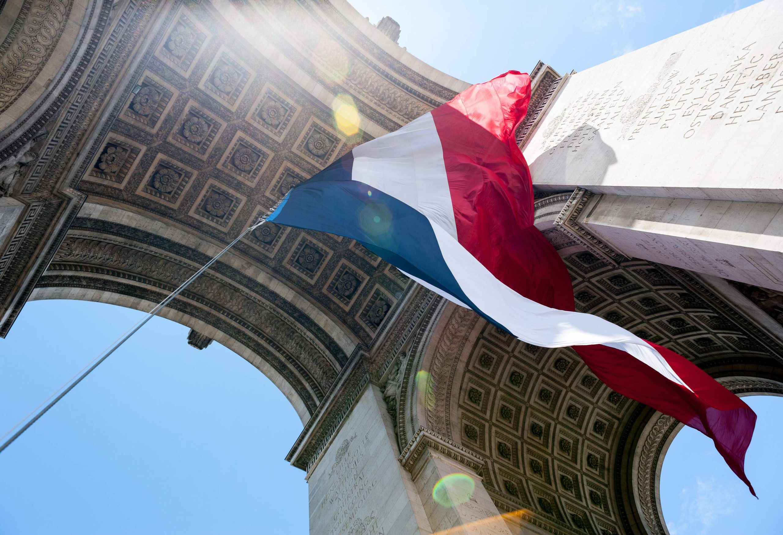 A waving French flag under the arch of a massive monument with intricately carved ceilings and walls.