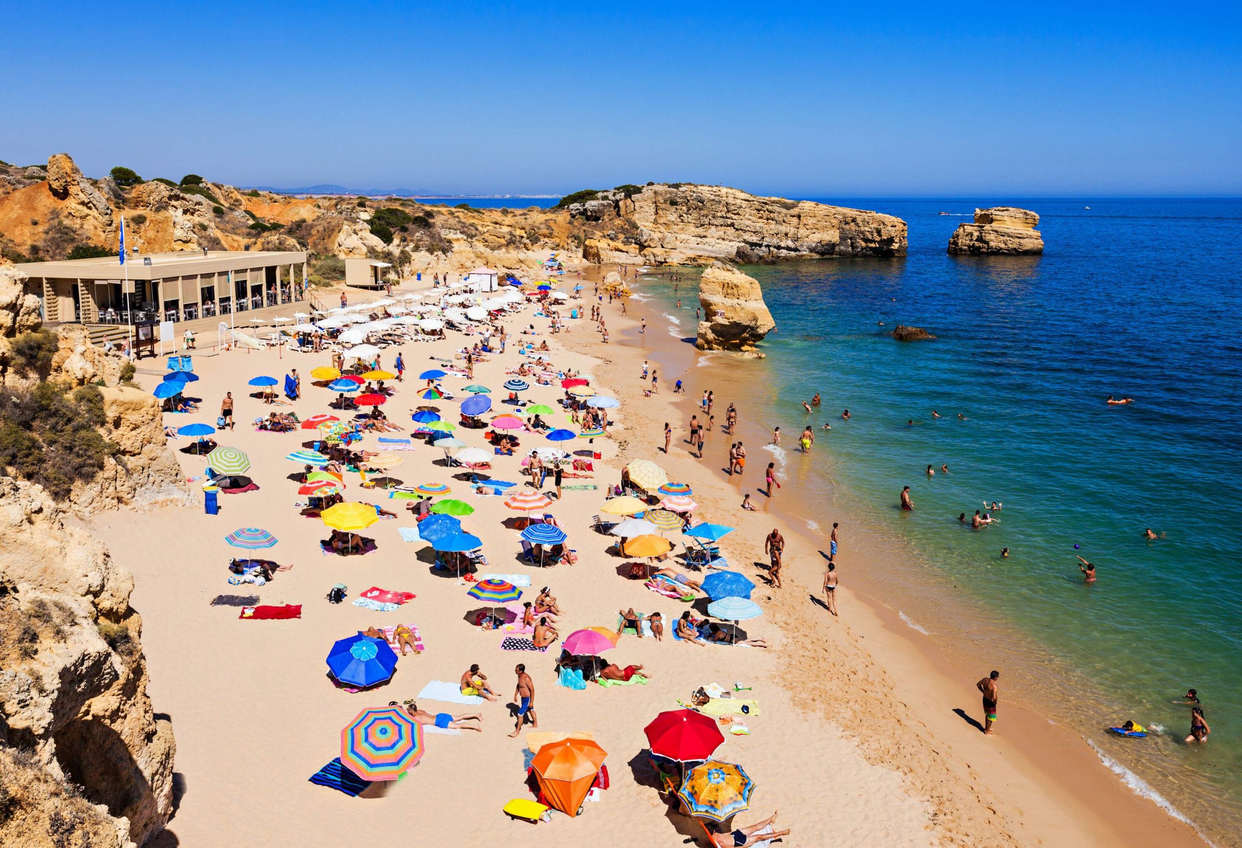 A balmy day on the beach with people playing in the water and relaxing on the sand under colourful umbrellas.