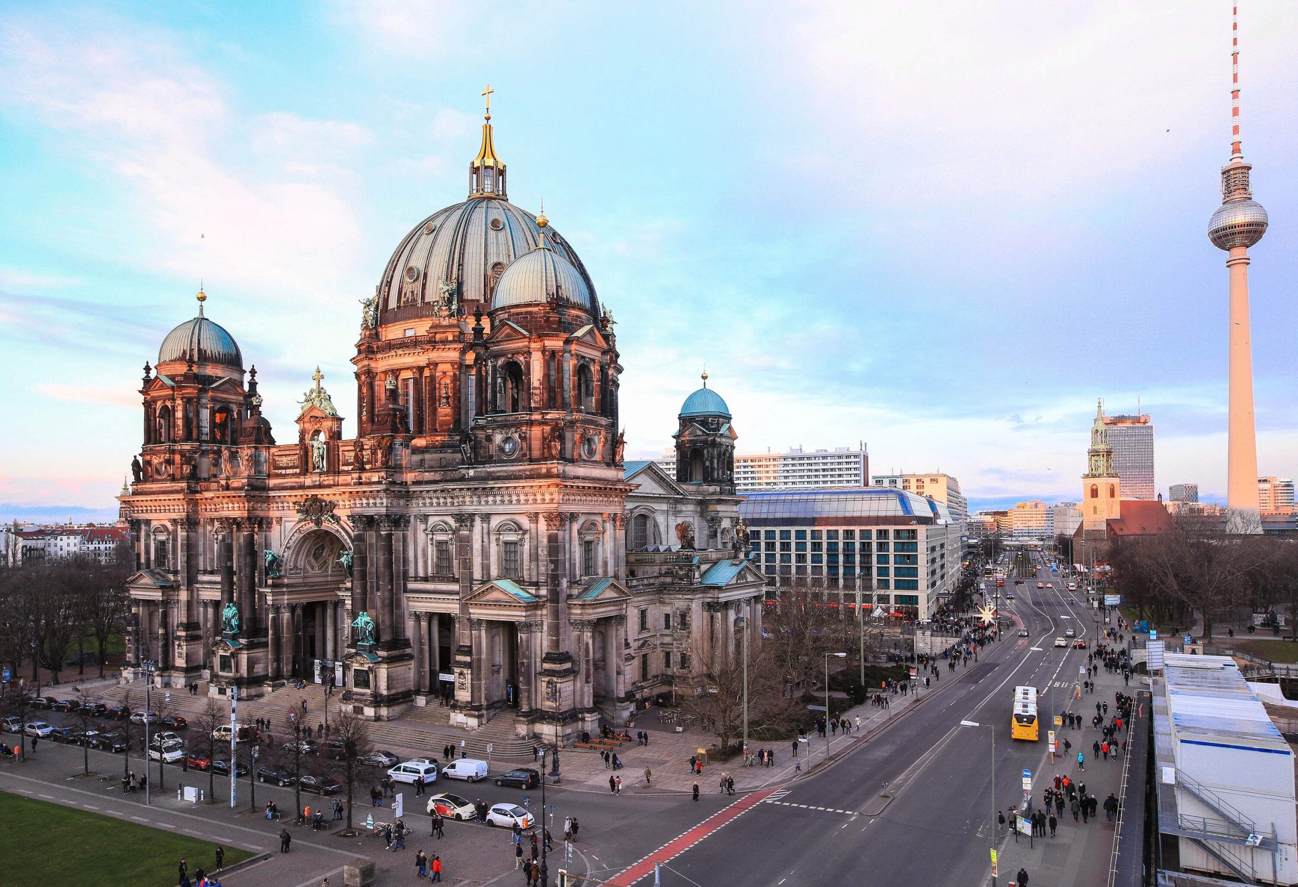 The street in front of the castle-like Berlin Cathedral is bustling with people and cars during the day.