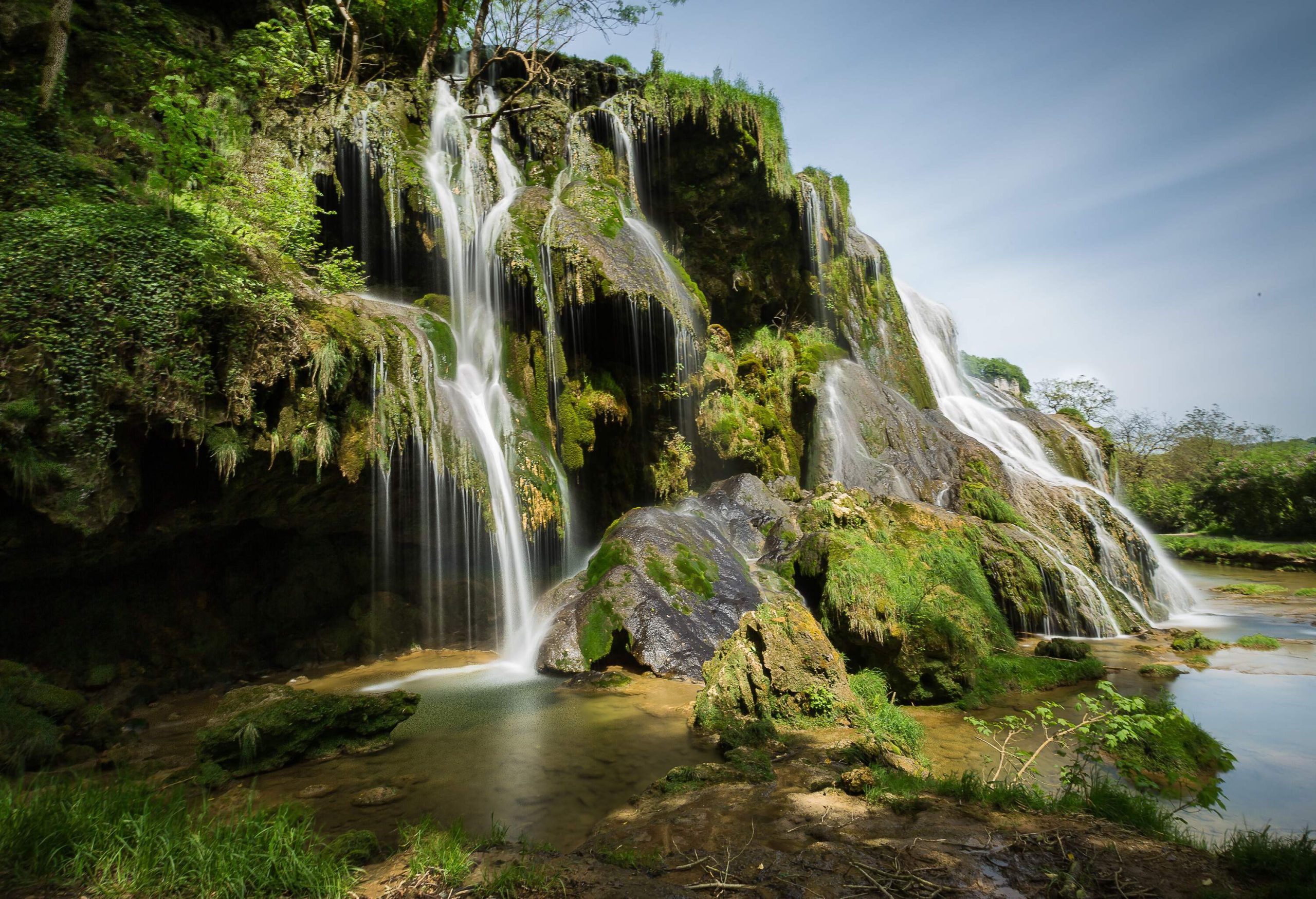 A waterfall plunges over a mossy ledge into a murky pool below.