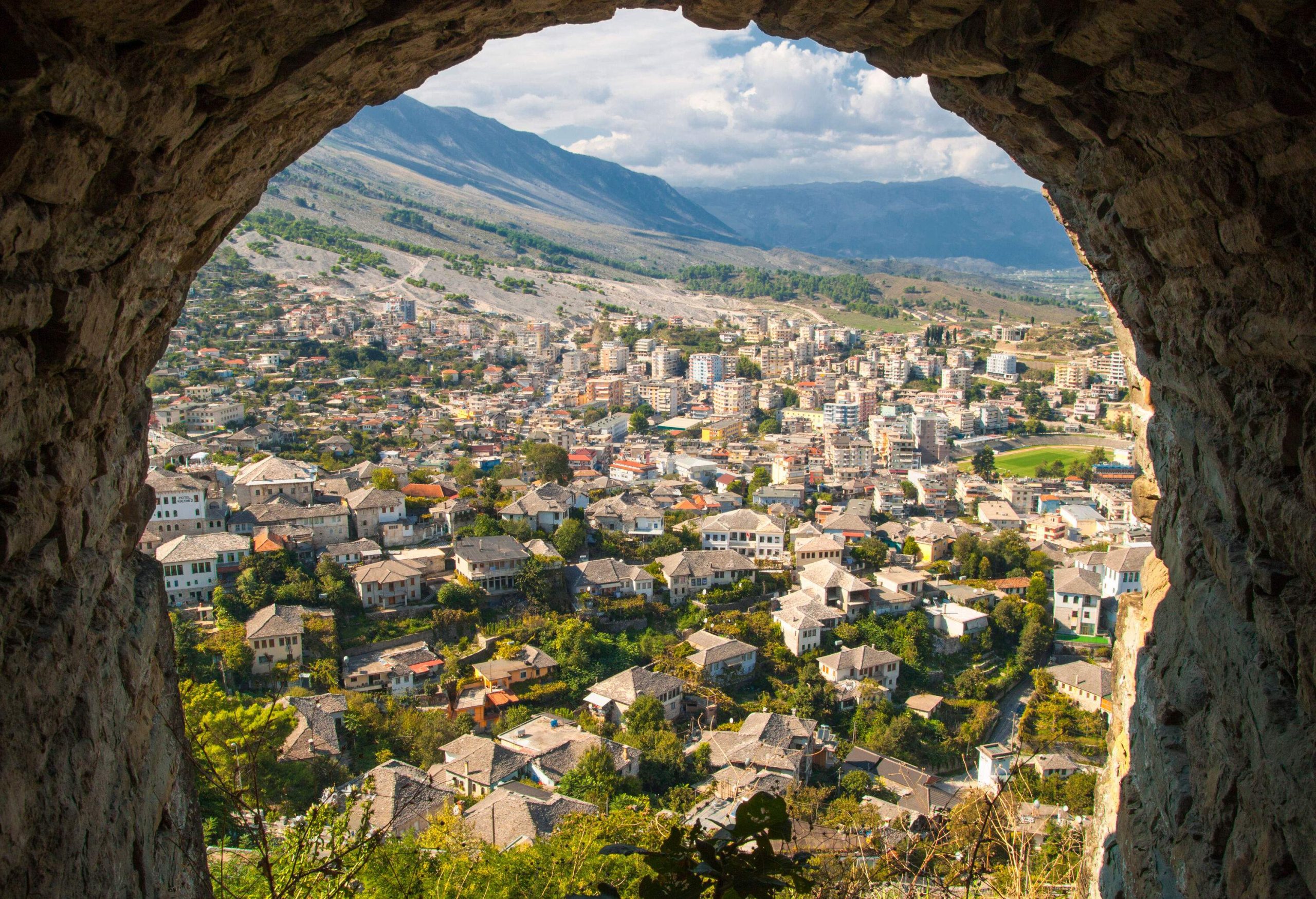The cityscape sloping at the base of the surrounding mountains viewed from a stone arch.