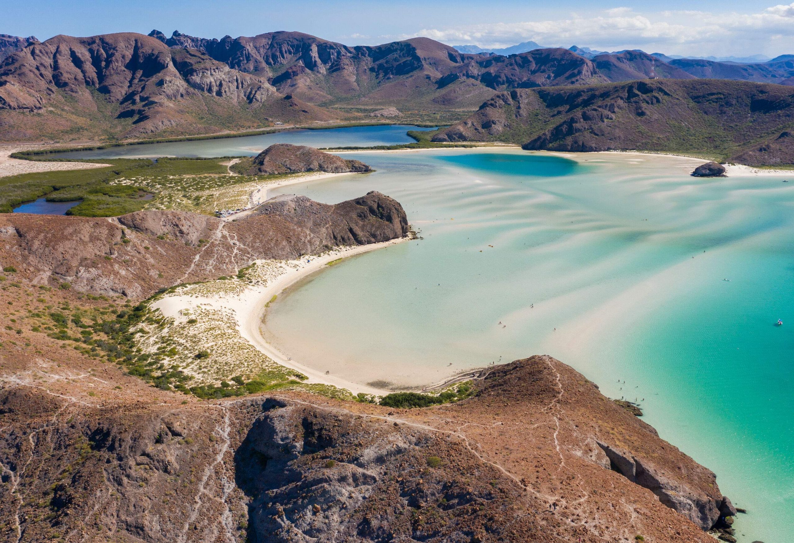 A picturesque cove beach with shallow turquoise waters surrounded by rock mountains. 