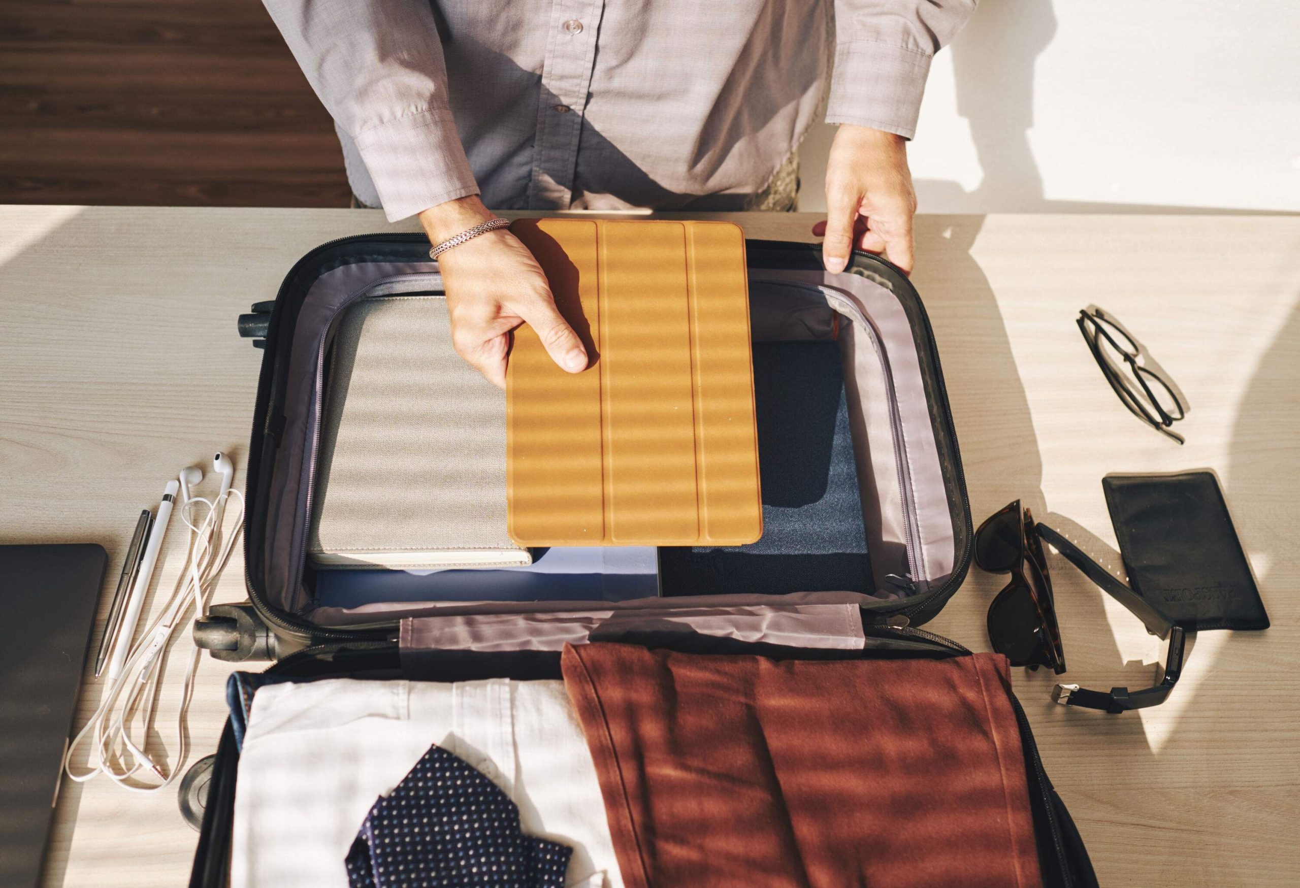 An individual puts an iPad inside a suitcase of his belongings.
