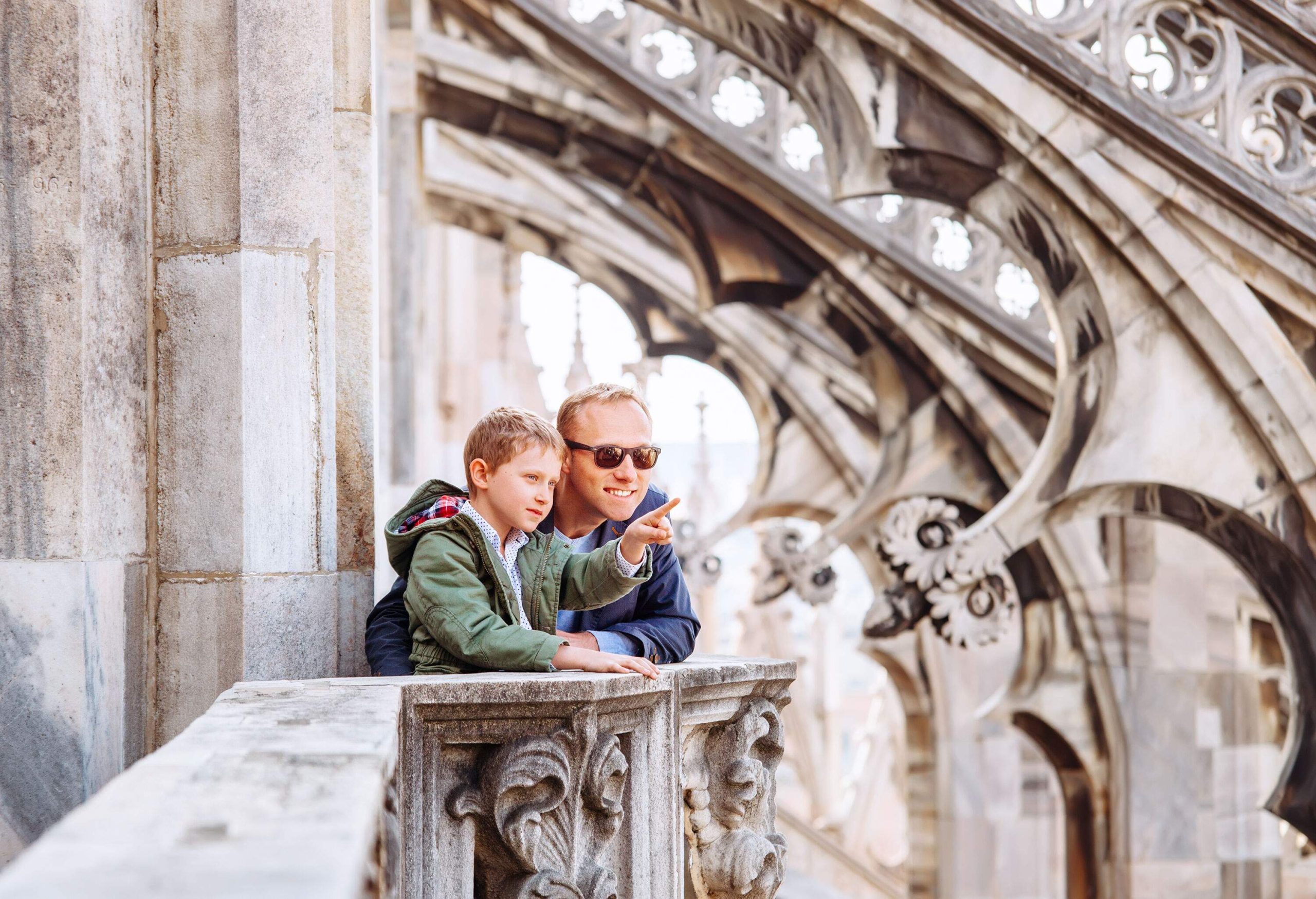 A son points something to his father while standing on the rooftop terrace of a majestic church.
