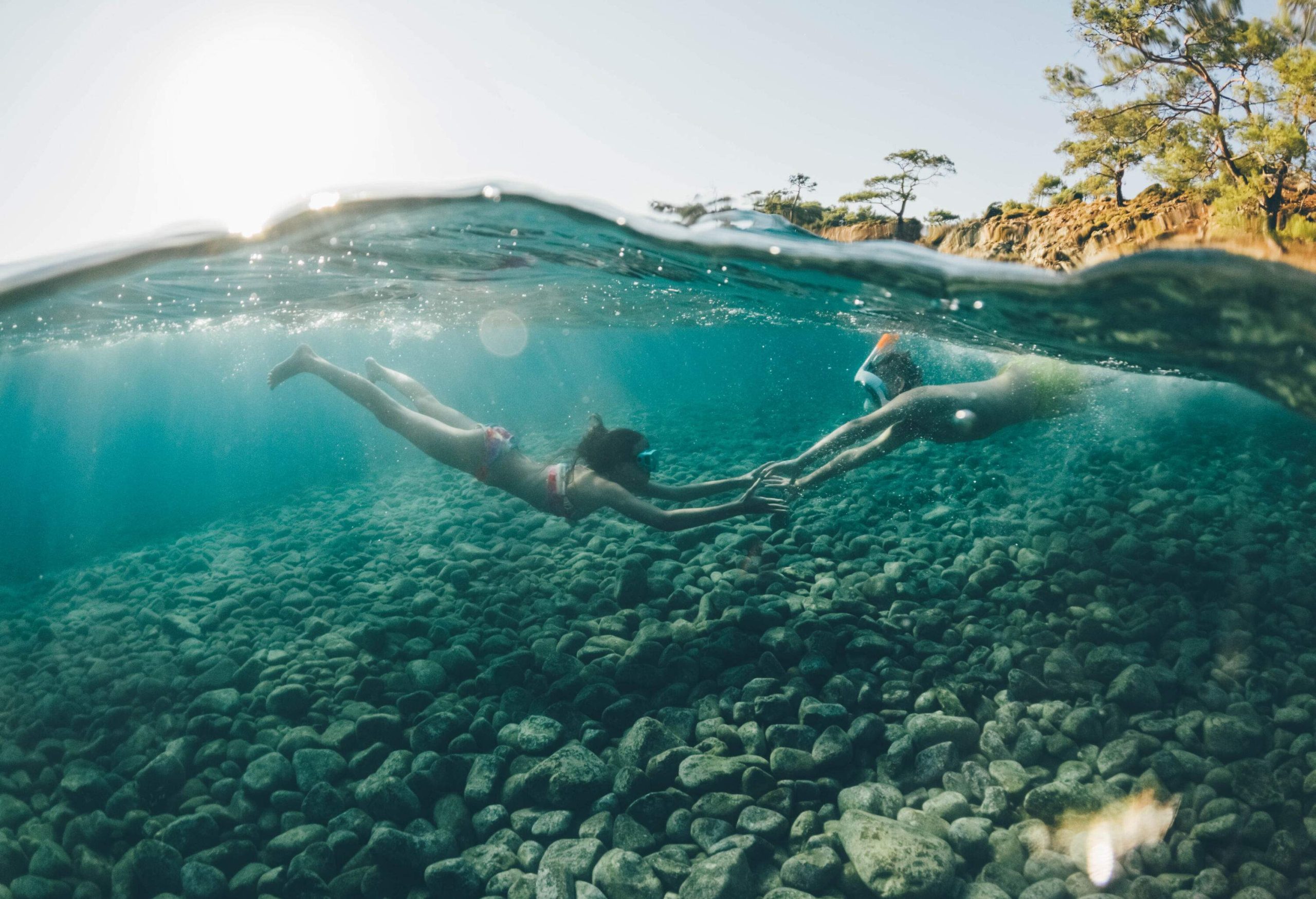 Underwater photo of two people reaching each under the rocky sea water.