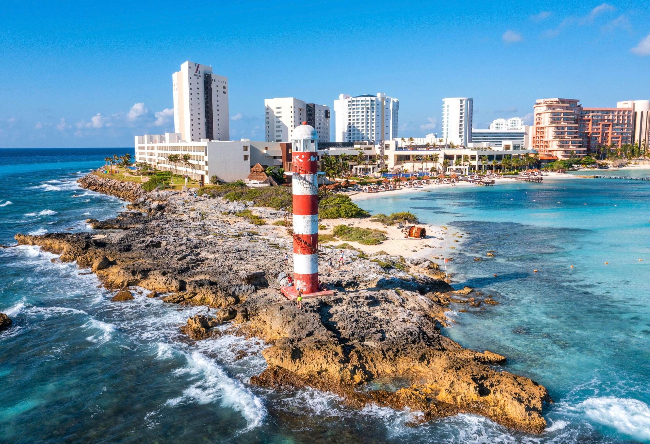 A lighthouse stands proudly at the edge of a rocky coastline, juxtaposed against a backdrop of modern coastal urban scenery, all embraced by the expansive blue sea.