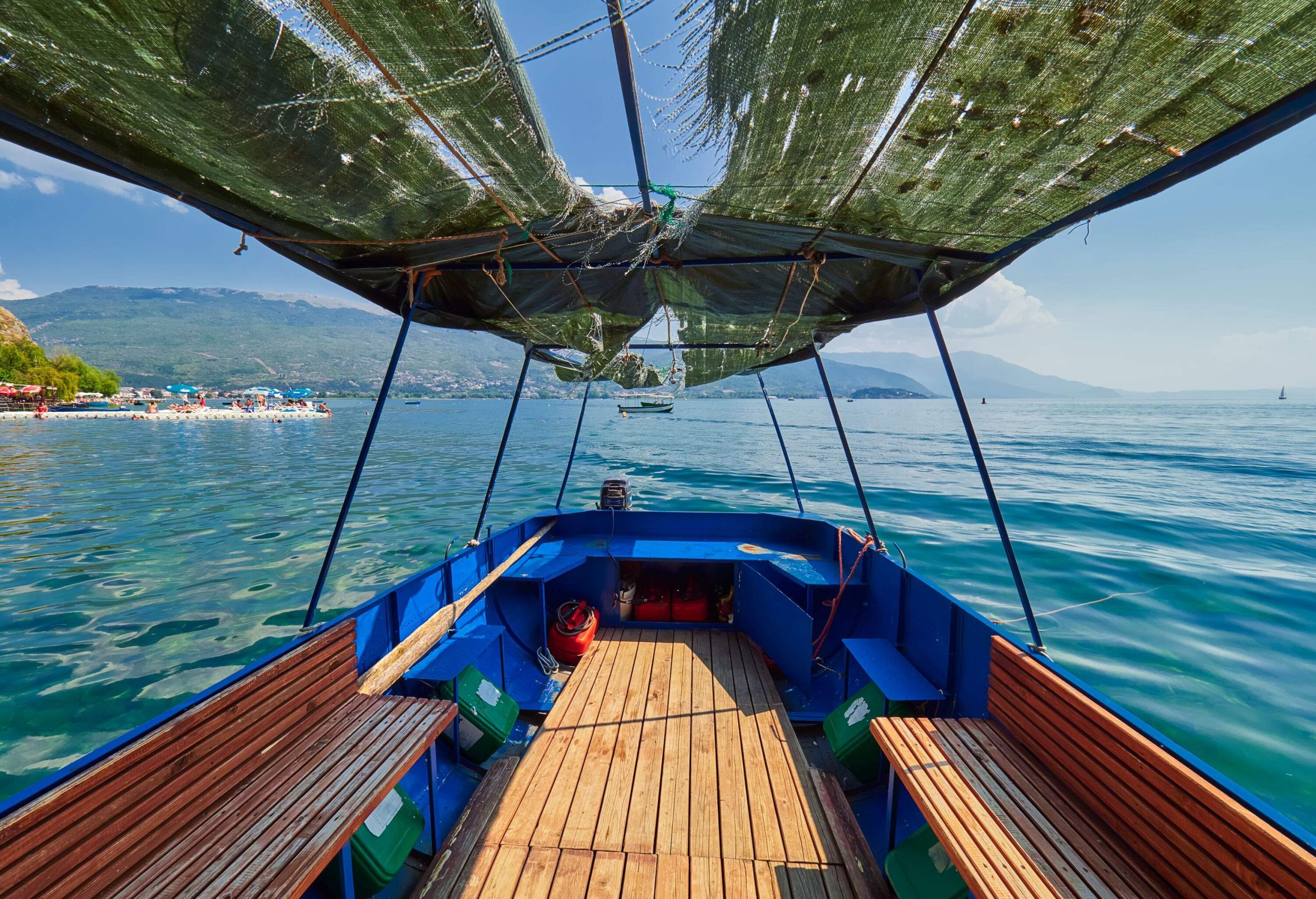 The inside of a boat with wooden floors and seats floating in a lake.
