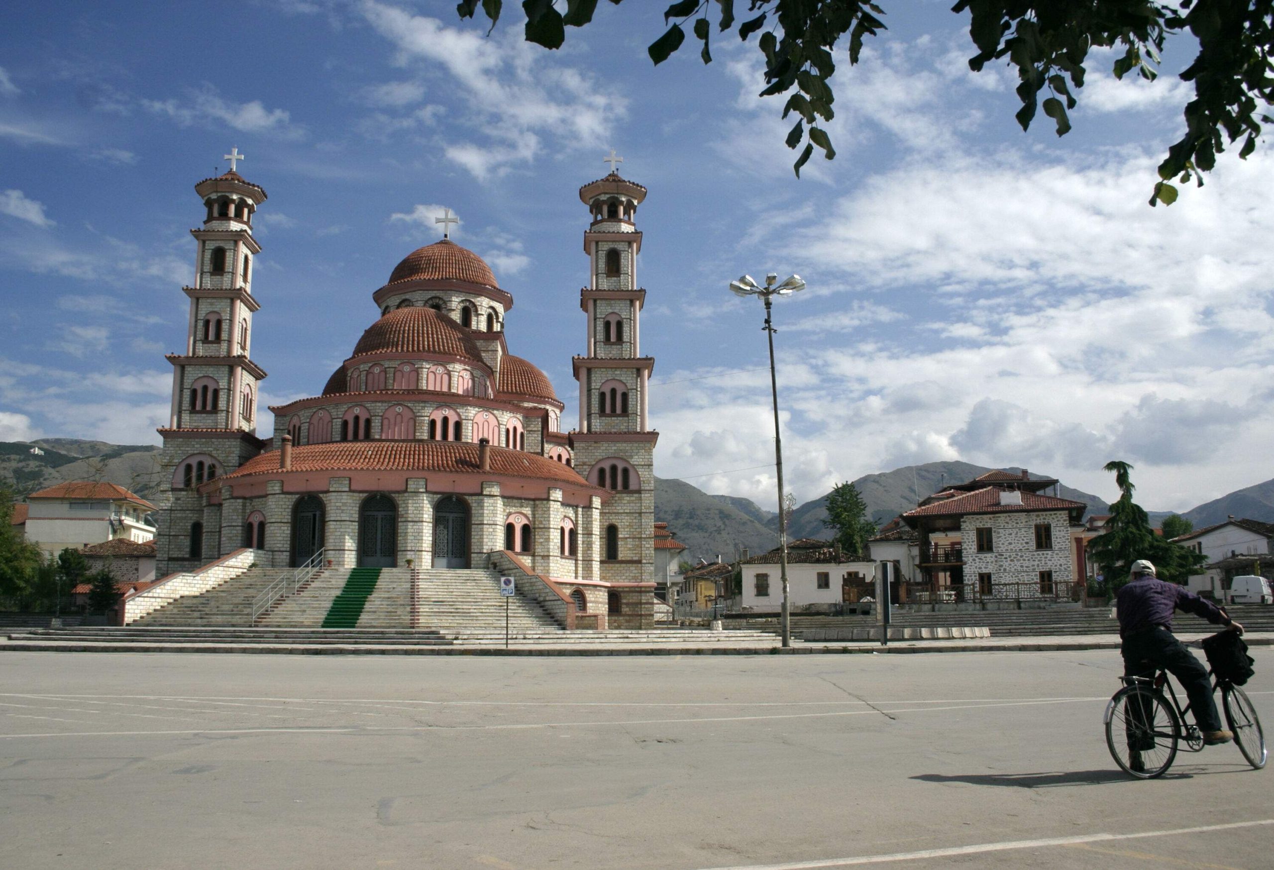 A person on a bicycle pauses to admire the Resurrection Cathedral in Korçë, with its grand domed structure and elegant bell towers, standing as a symbol of faith and devotion.