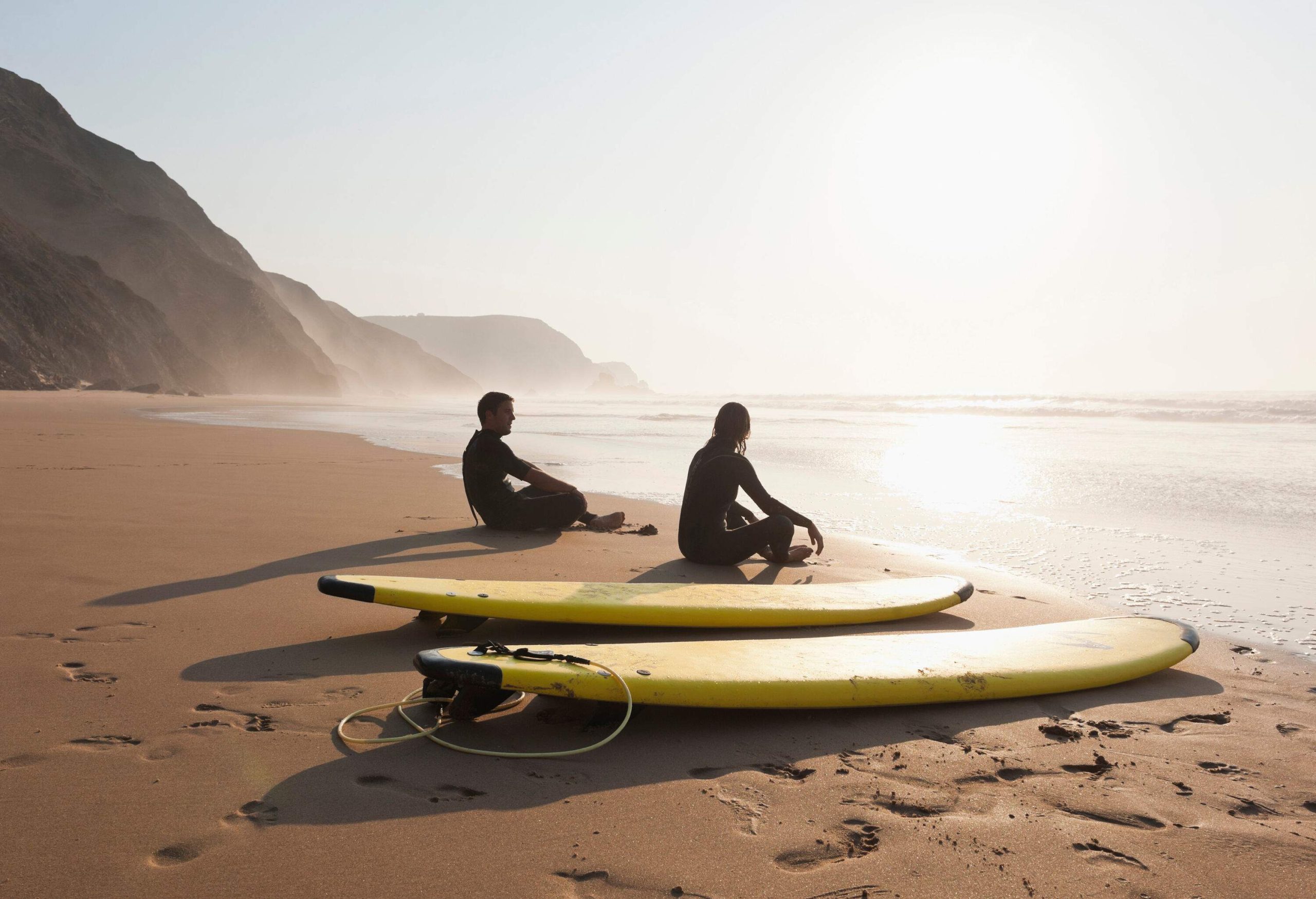 Two surfers sitting on the sand near their surfboards on the beach.