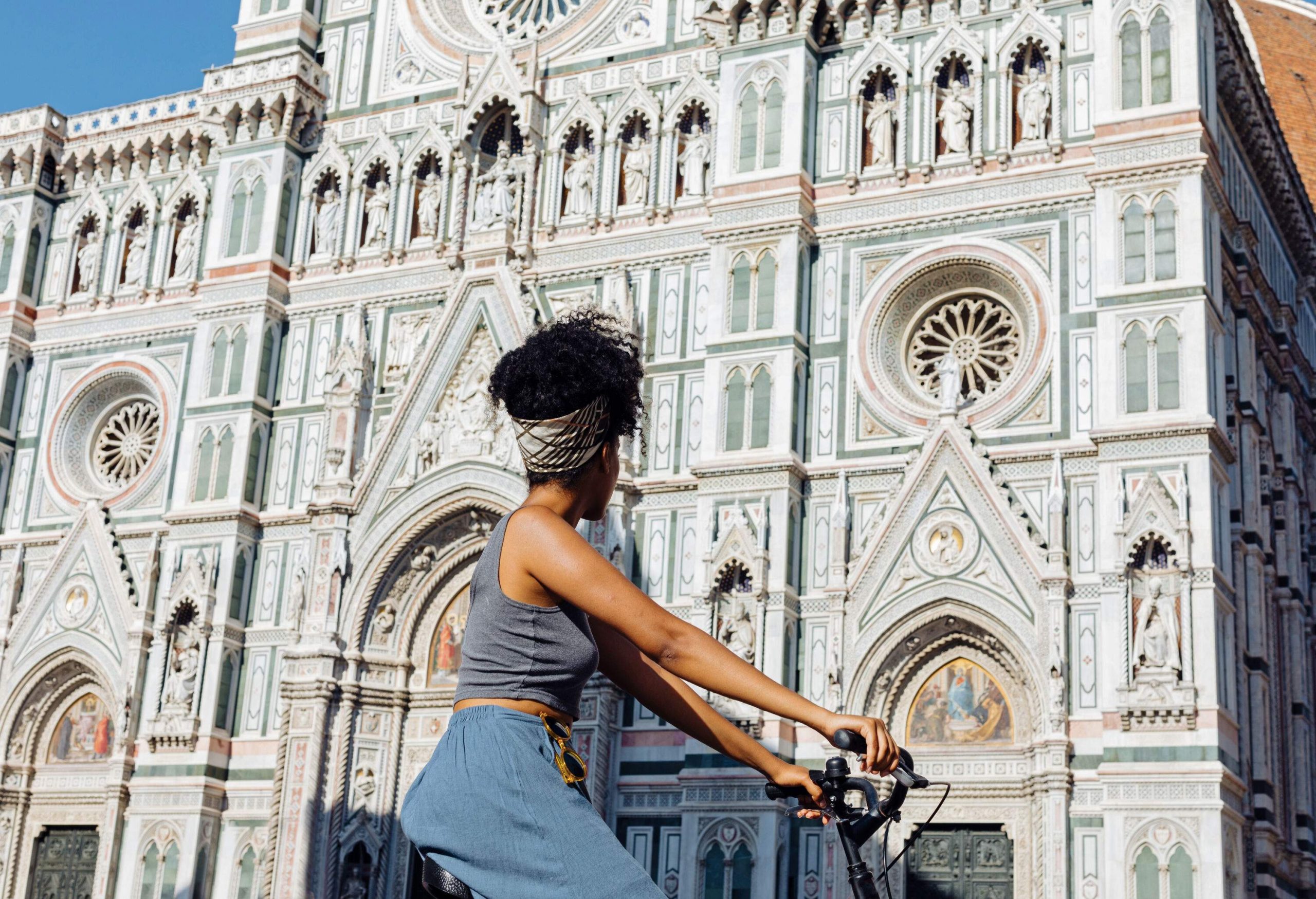 A trendy woman on a bike looking at the exquisite façade of the Florence Cathedral.