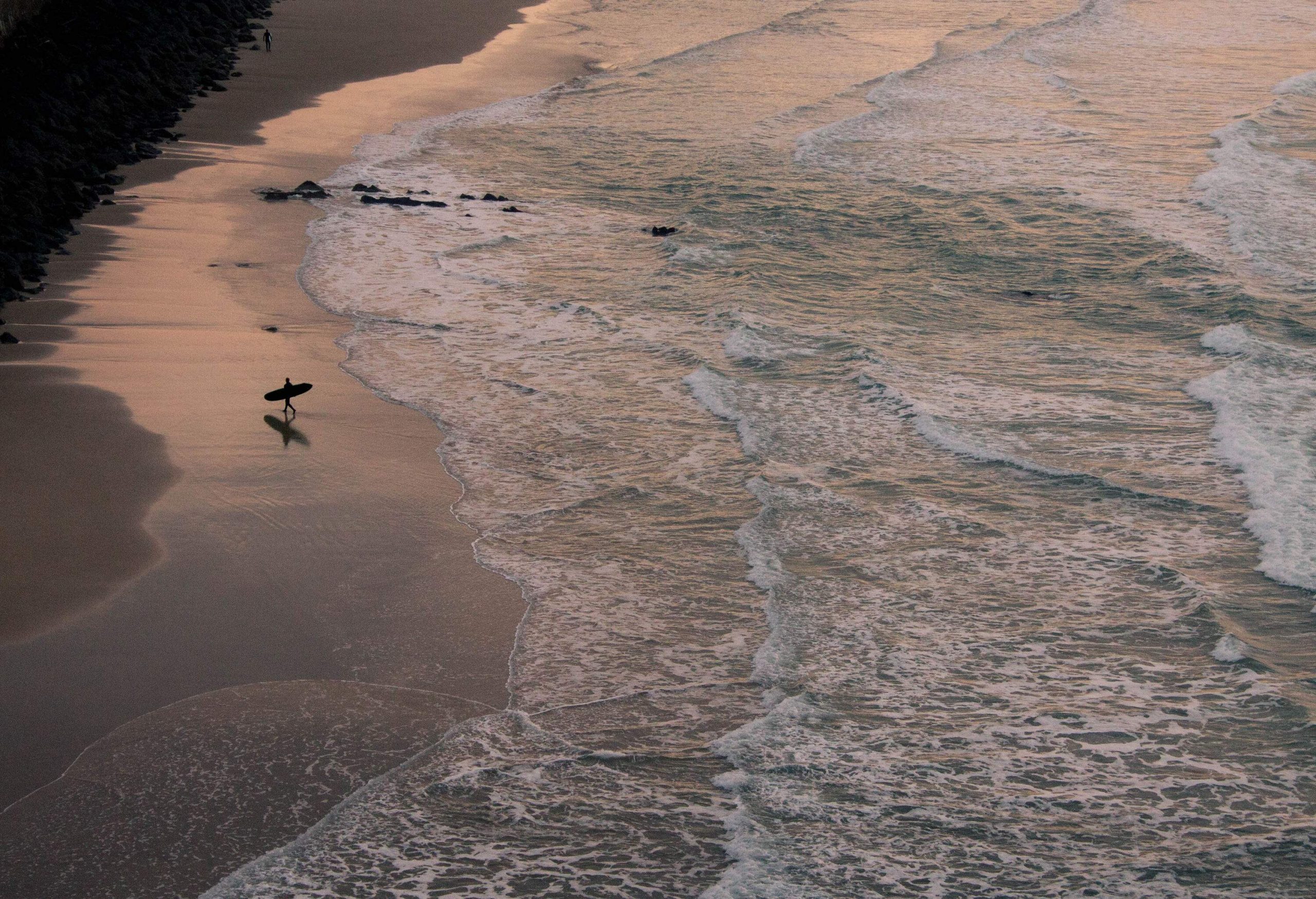 Silhouette of a surfer carrying a surfboard while walking away from a beach.