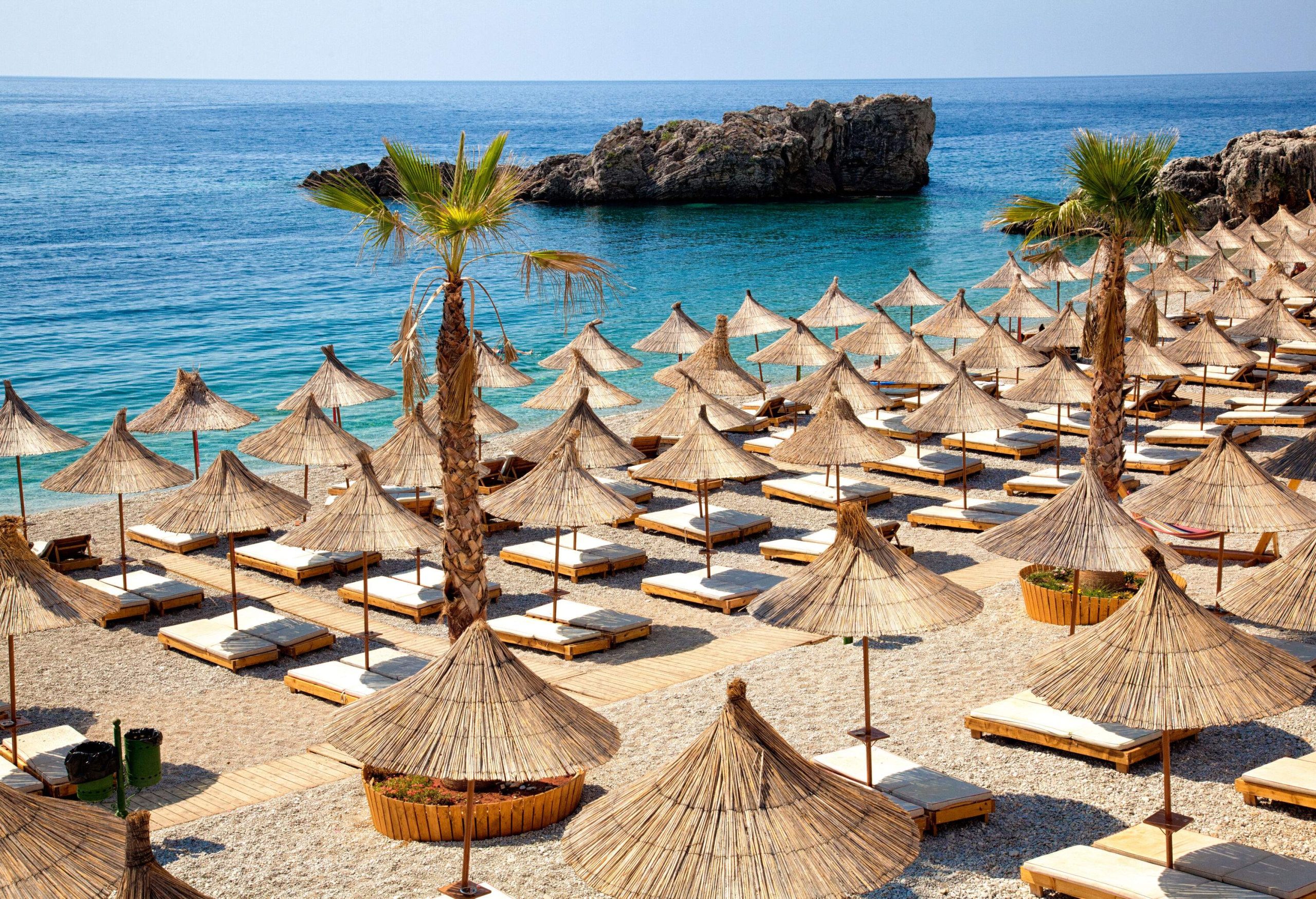 A beach with rows of sunbeds under thatched umbrellas.