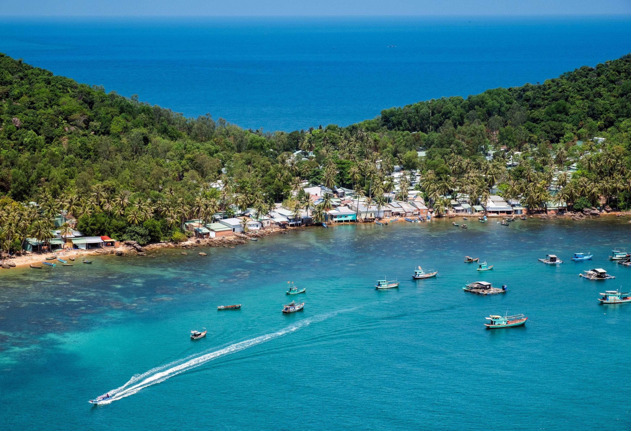 A picturesque village nestled on the slopes of a lush island, with moored boats dotting the serene coastline.