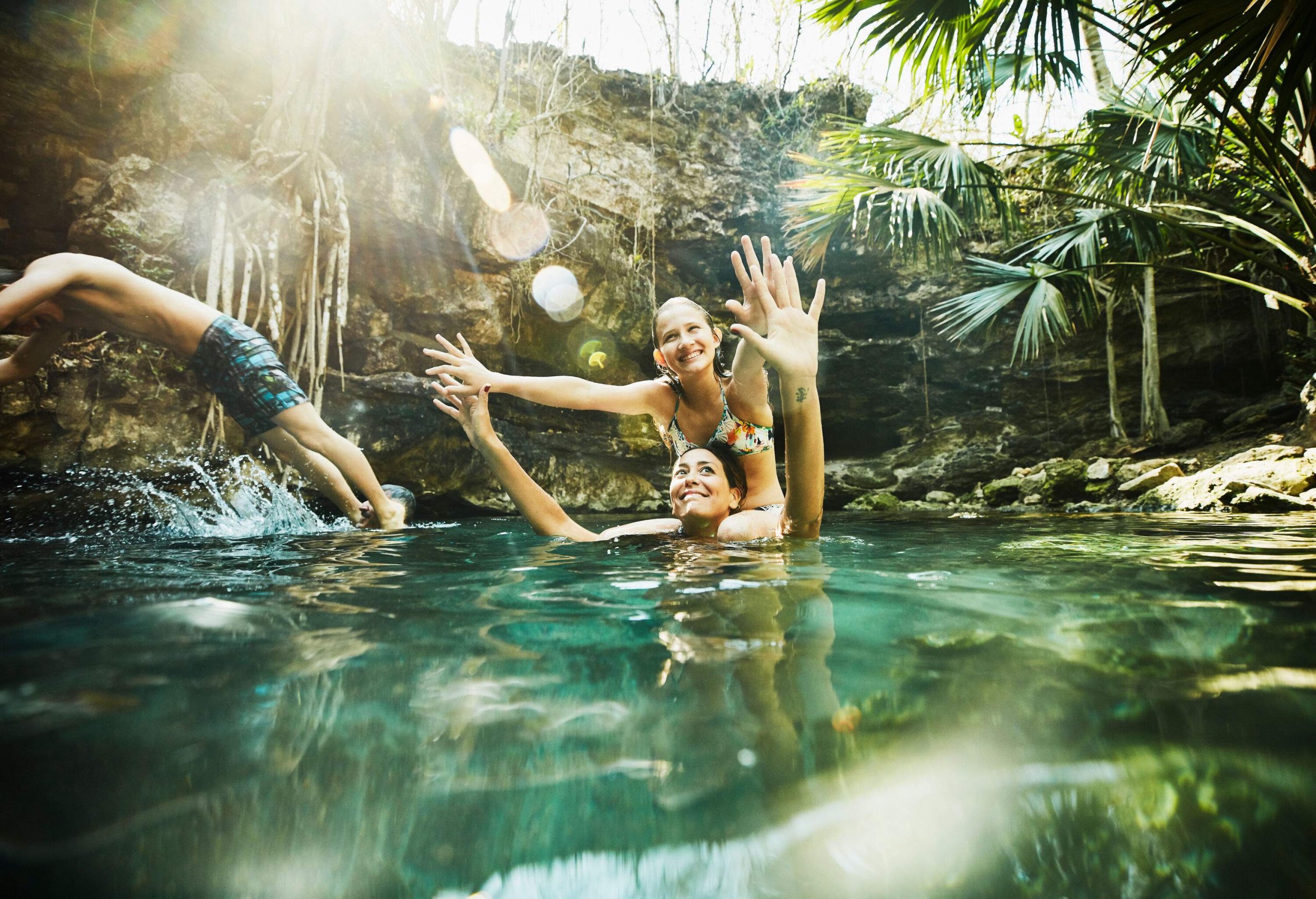 Woman in a bathing suit sits on the shoulders of someone who is submerged in water as someone dives next to them.