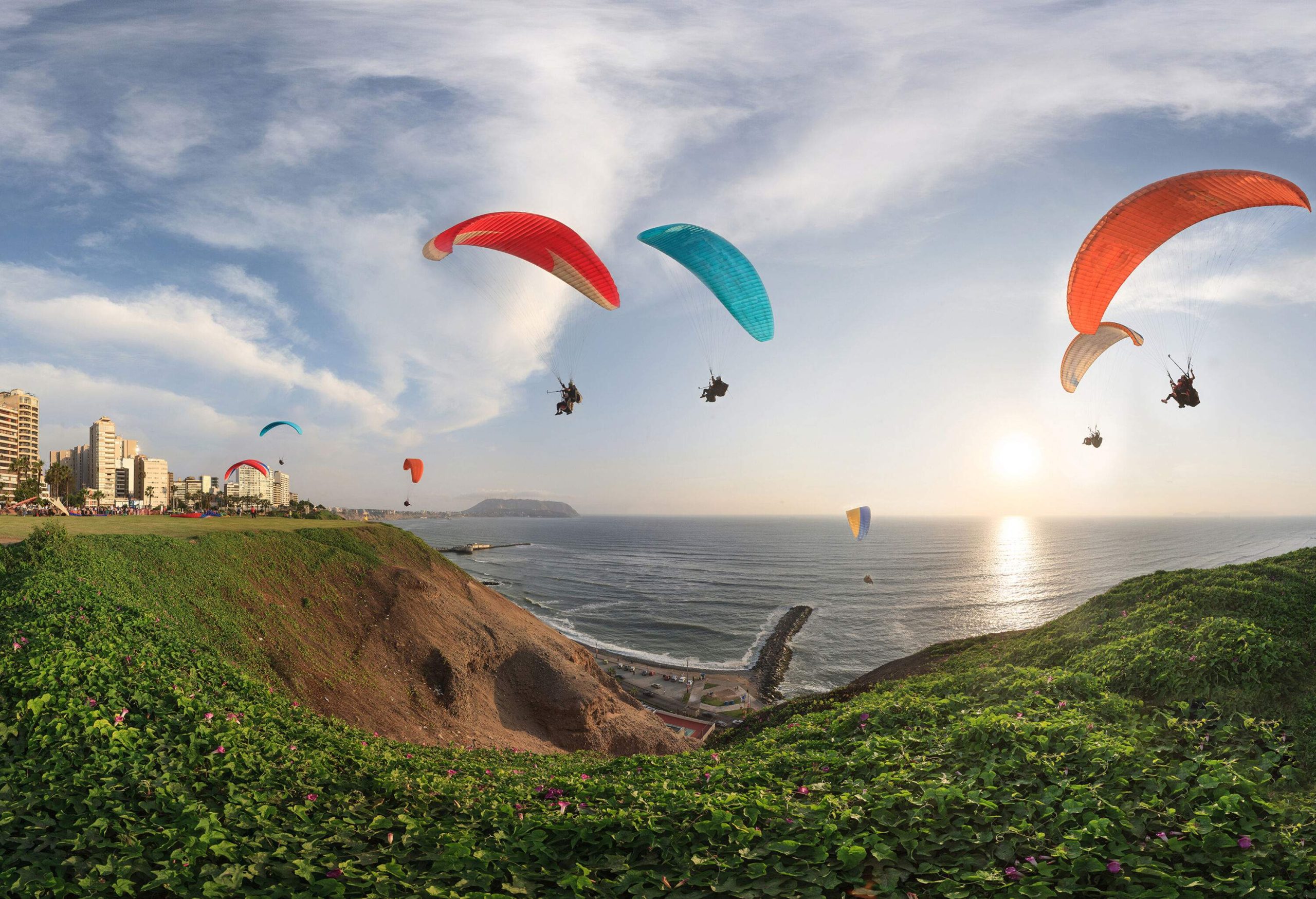 Colourful canopies of paragliders dotting the sky over the sea and surrounding cliffs.