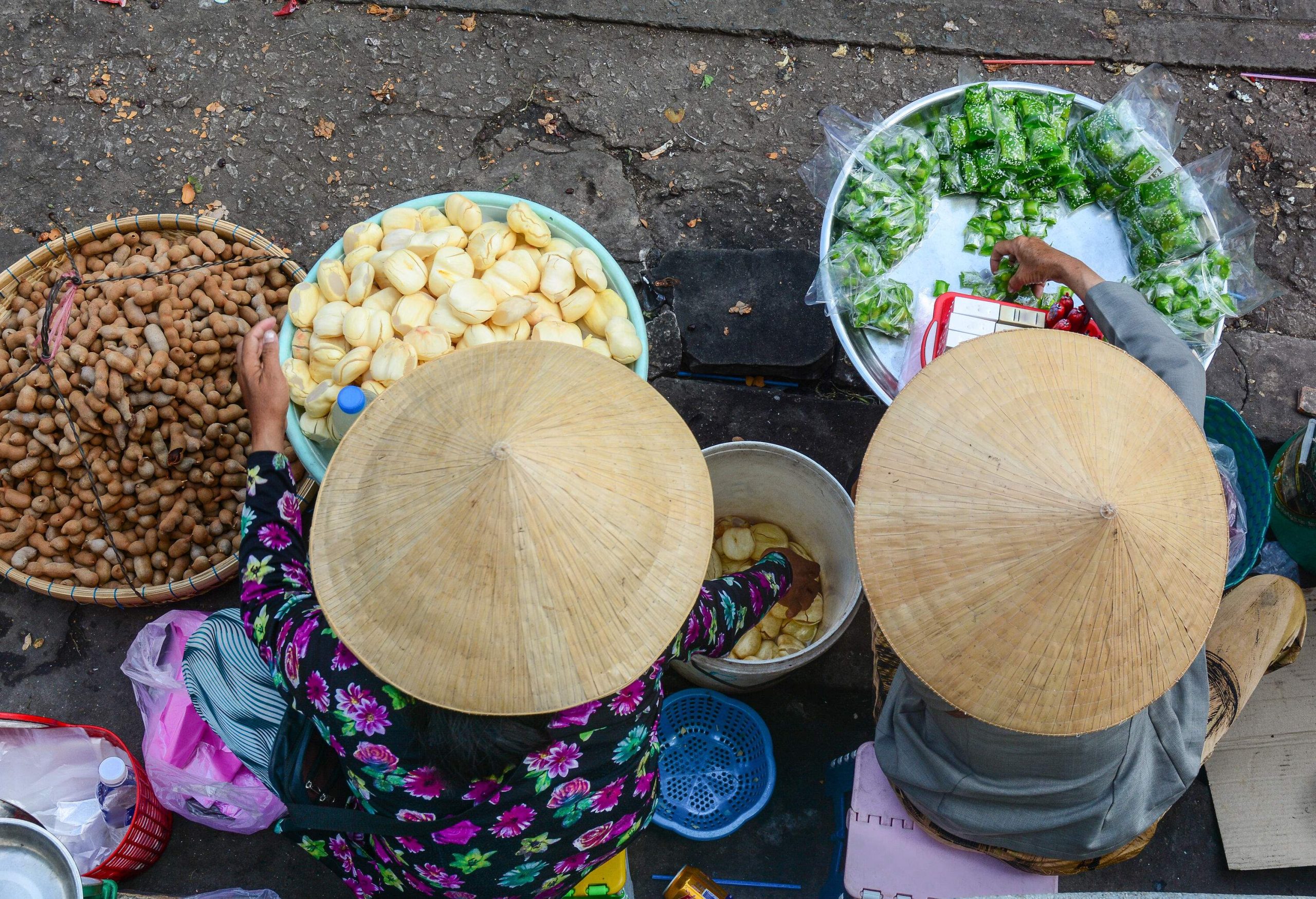 Vendors with big straw hats selling a variety of snacks on a street.
