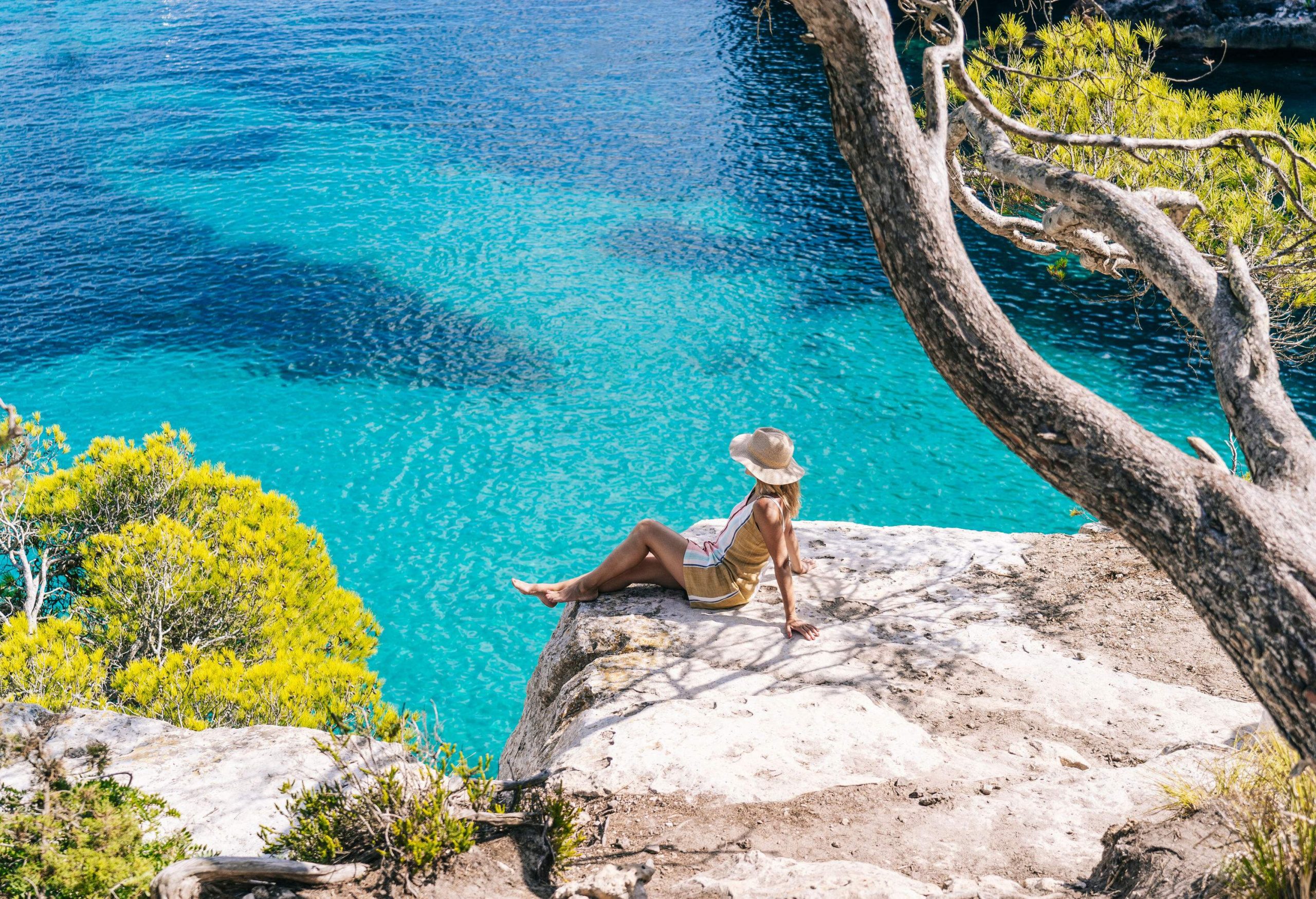 A woman sits on a cliff by the tranquil sea.