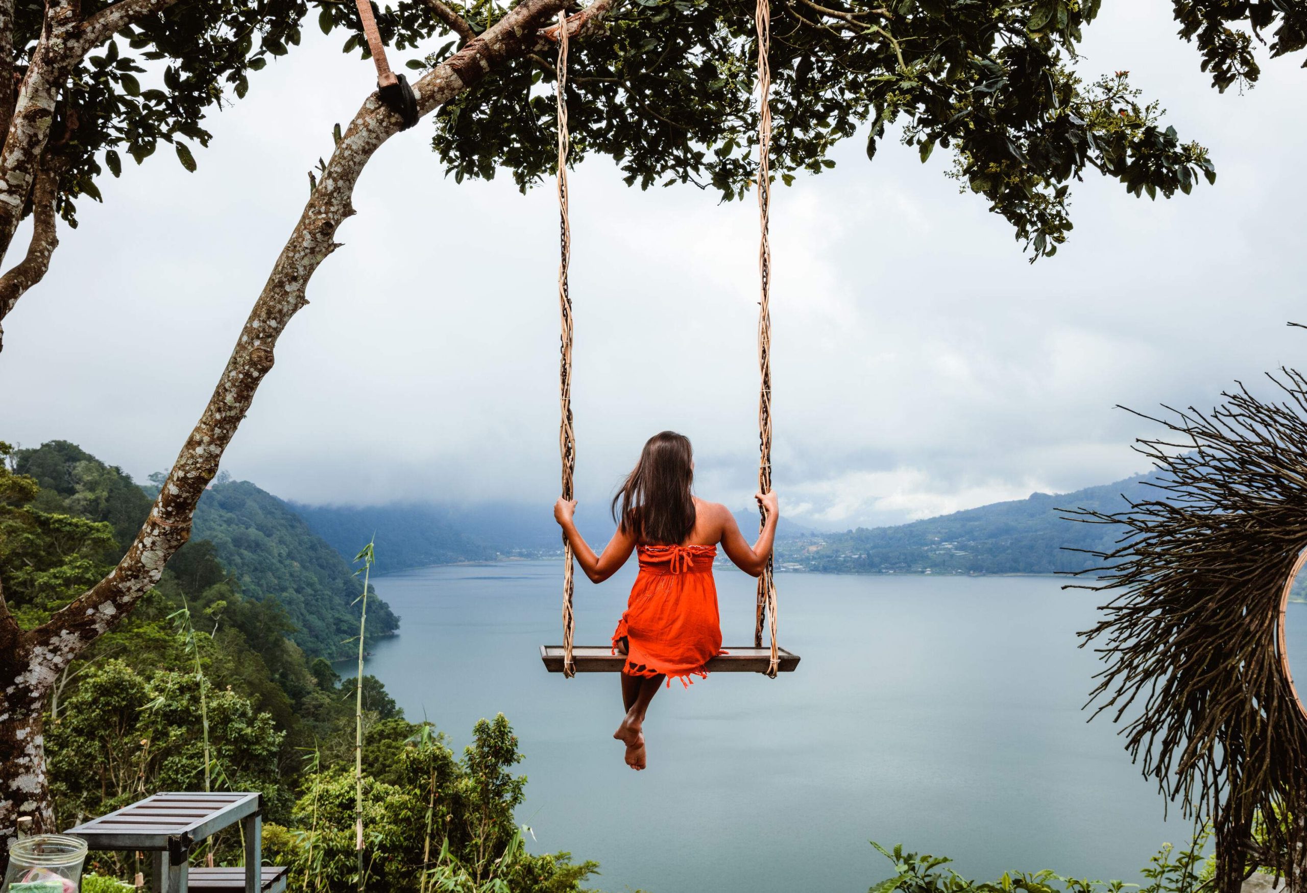 A woman sits on a swing that overlooks a huge lake.
