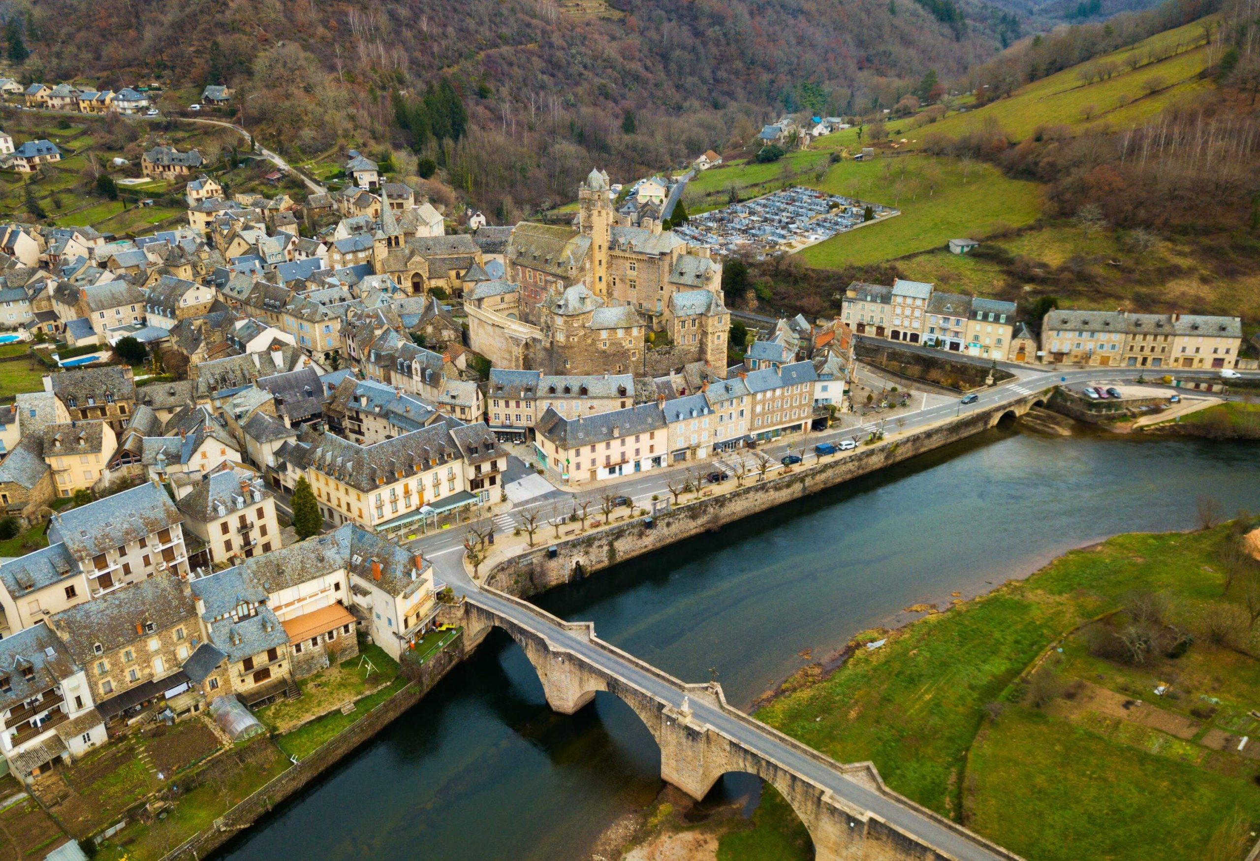 Aerial view of picturesque village of Estaing with medieval castle and gothique arched bridge across Lot river, Aveyron, France