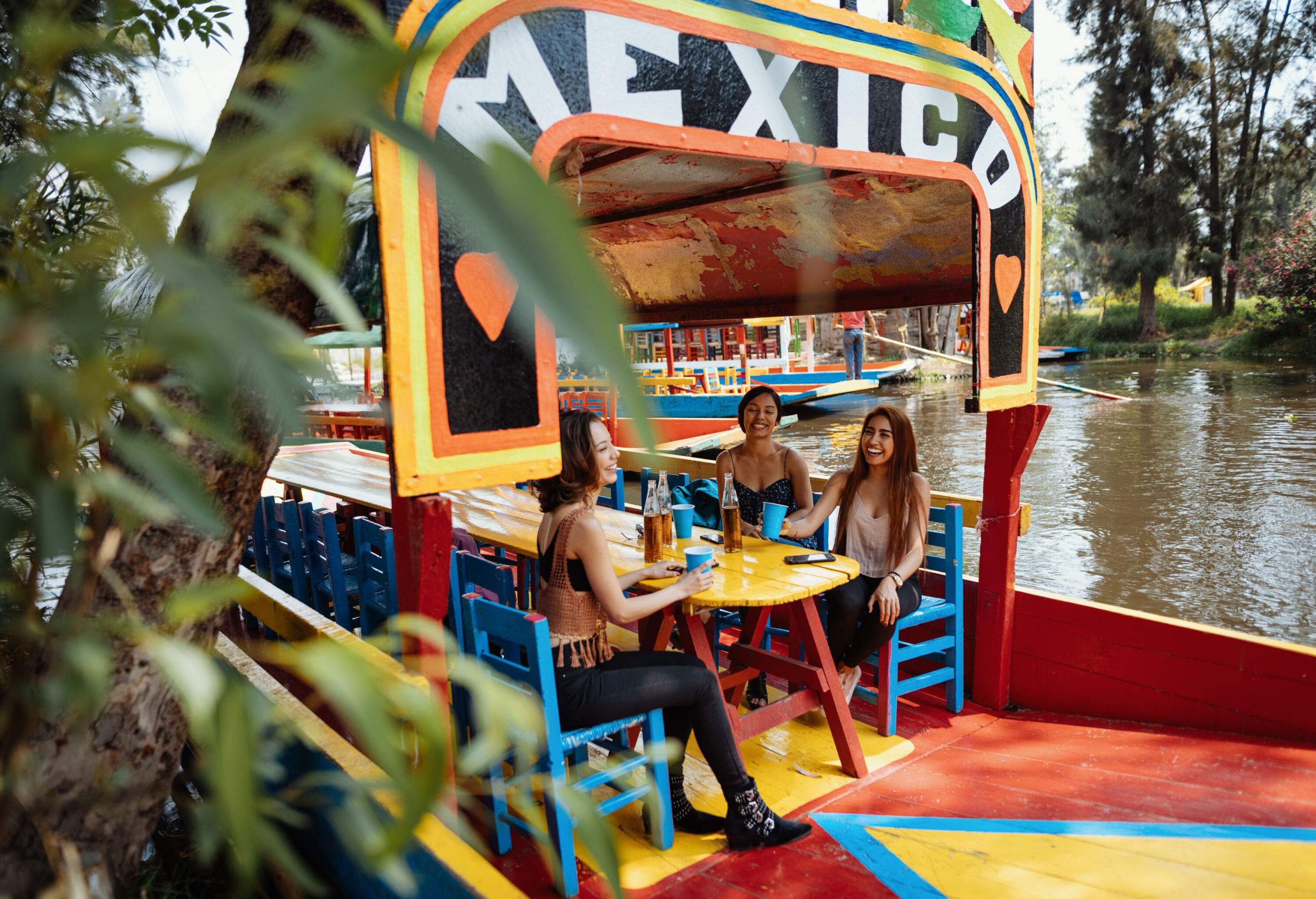 Three joyful women in a colourful restaurant boat enjoy their glasses of beer.