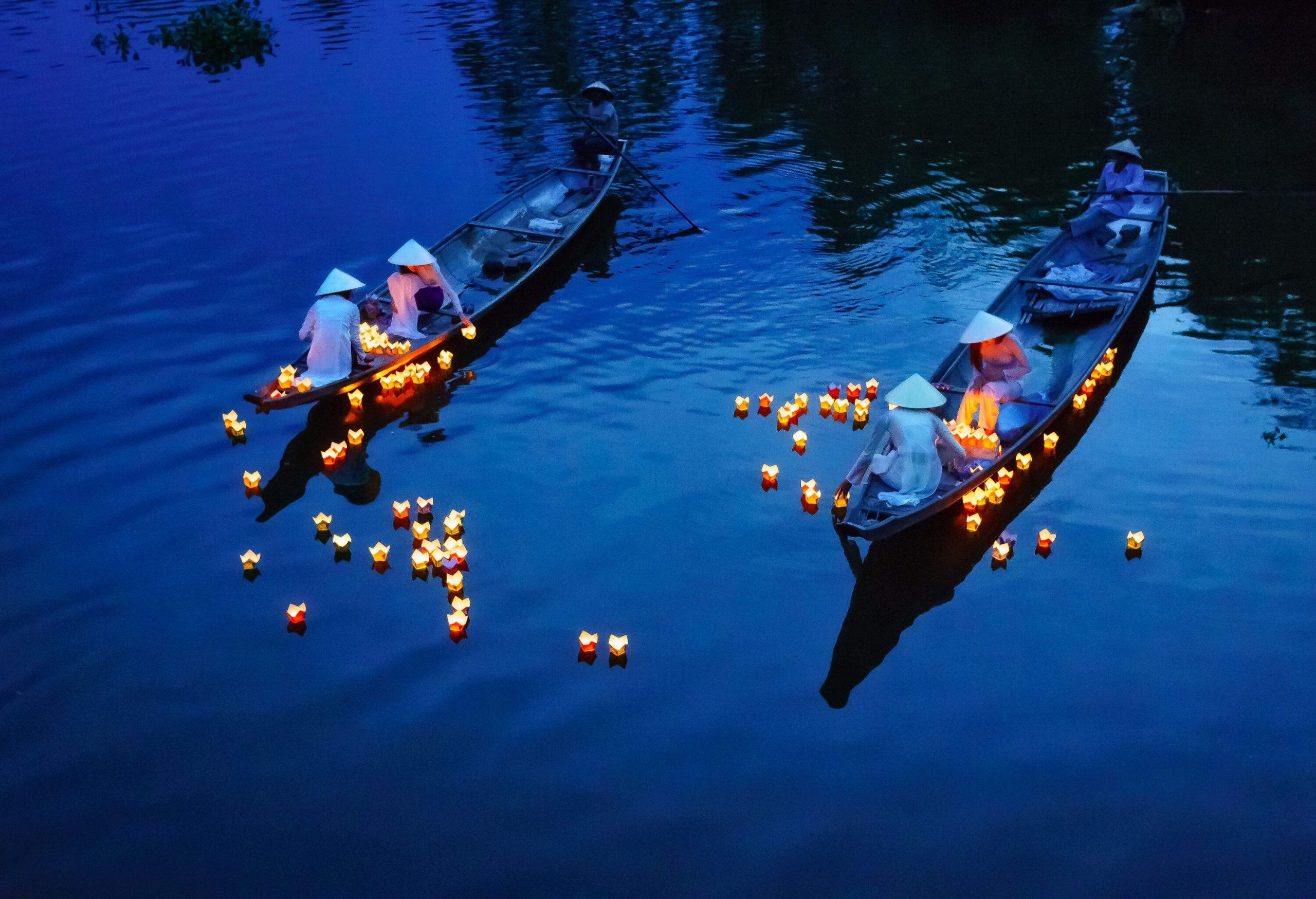 Girls wearing traditional sakkat and elegant Ao Dai dresses release floating candles onto the river from their boats.