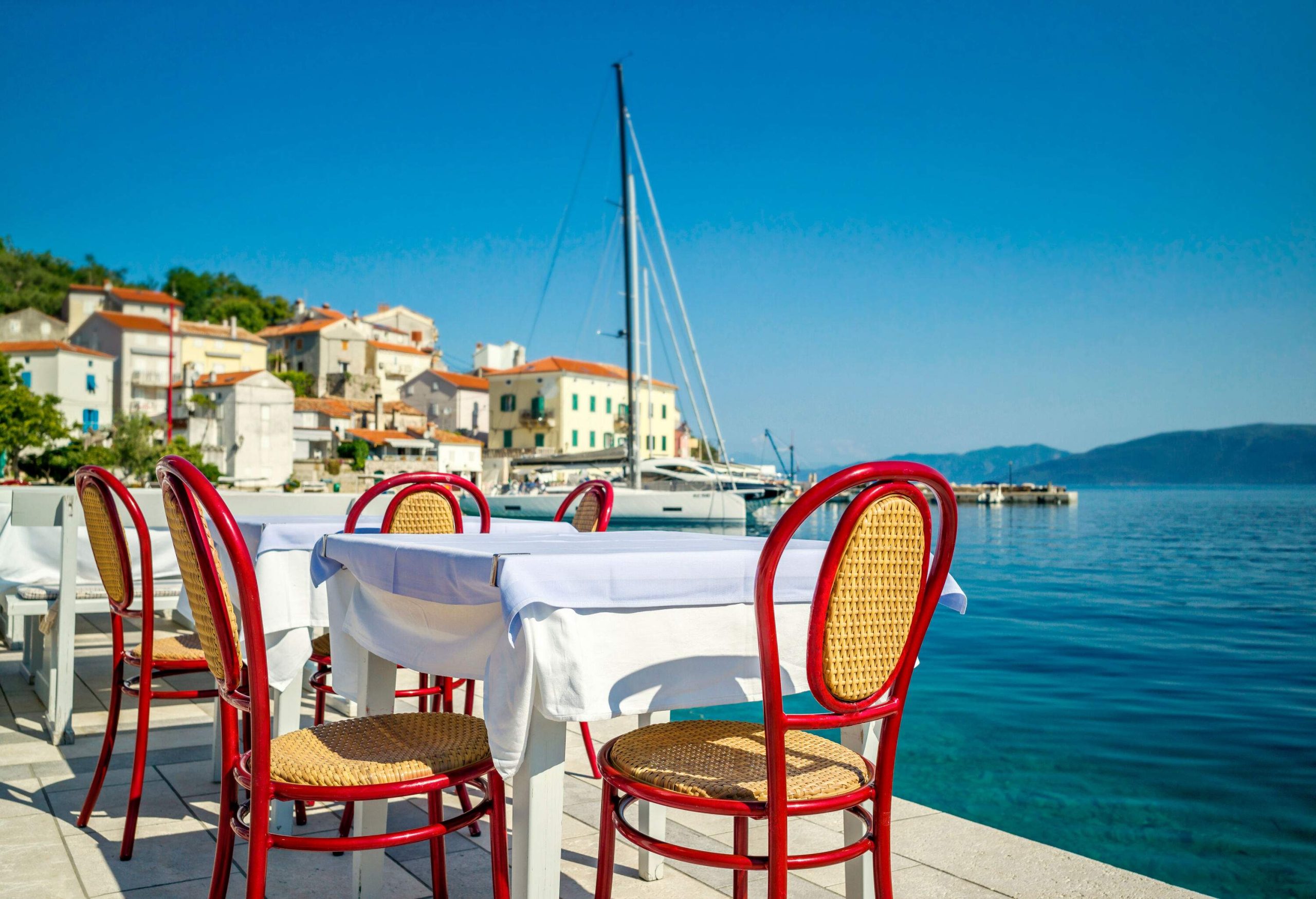 Tables and chairs are ready for outdoor dining alongside the harbour with a view of houses layered on the hill.