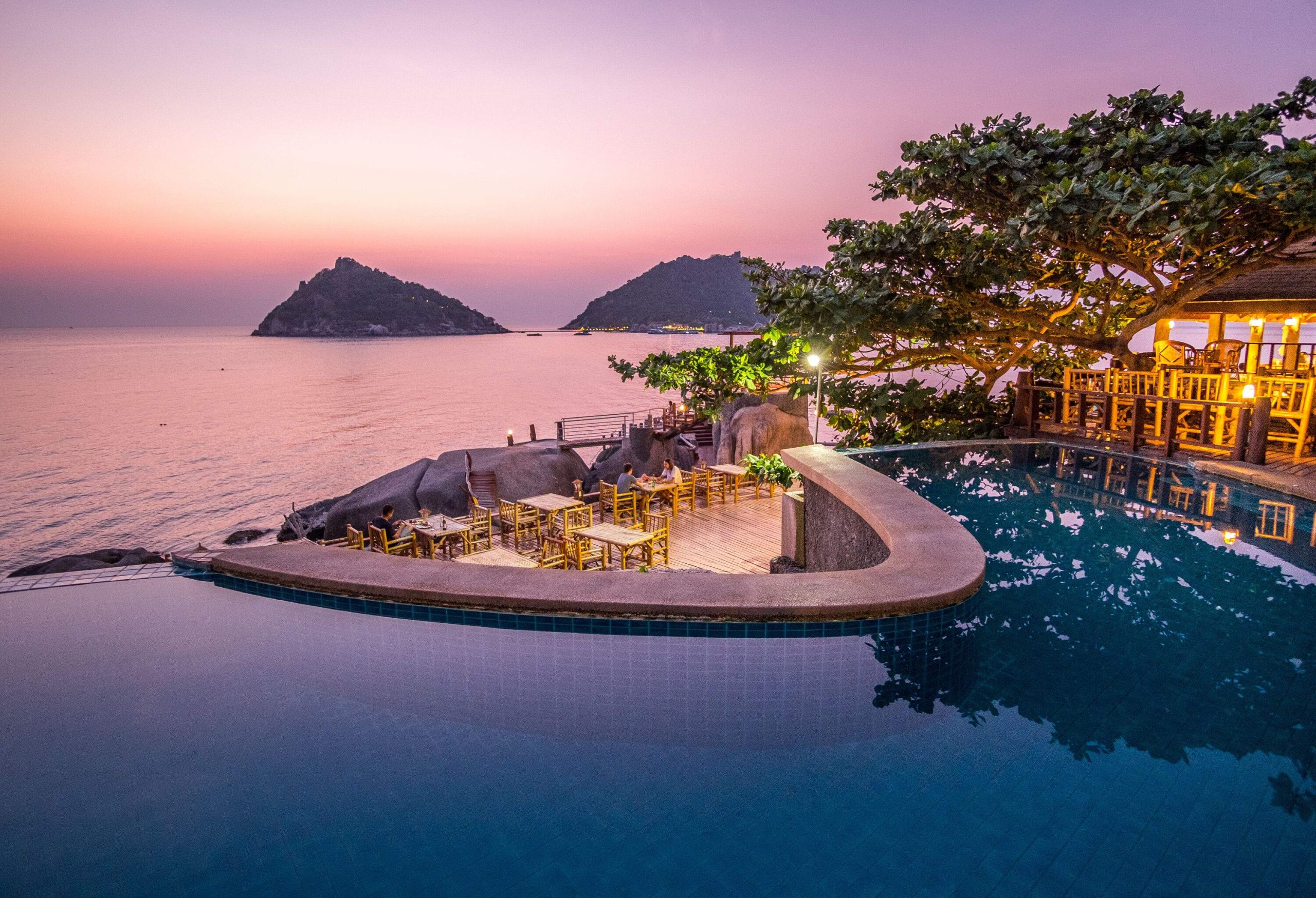 A resort pool and outdoor dining overlooking the picturesque sea against the scenic twilight sky.