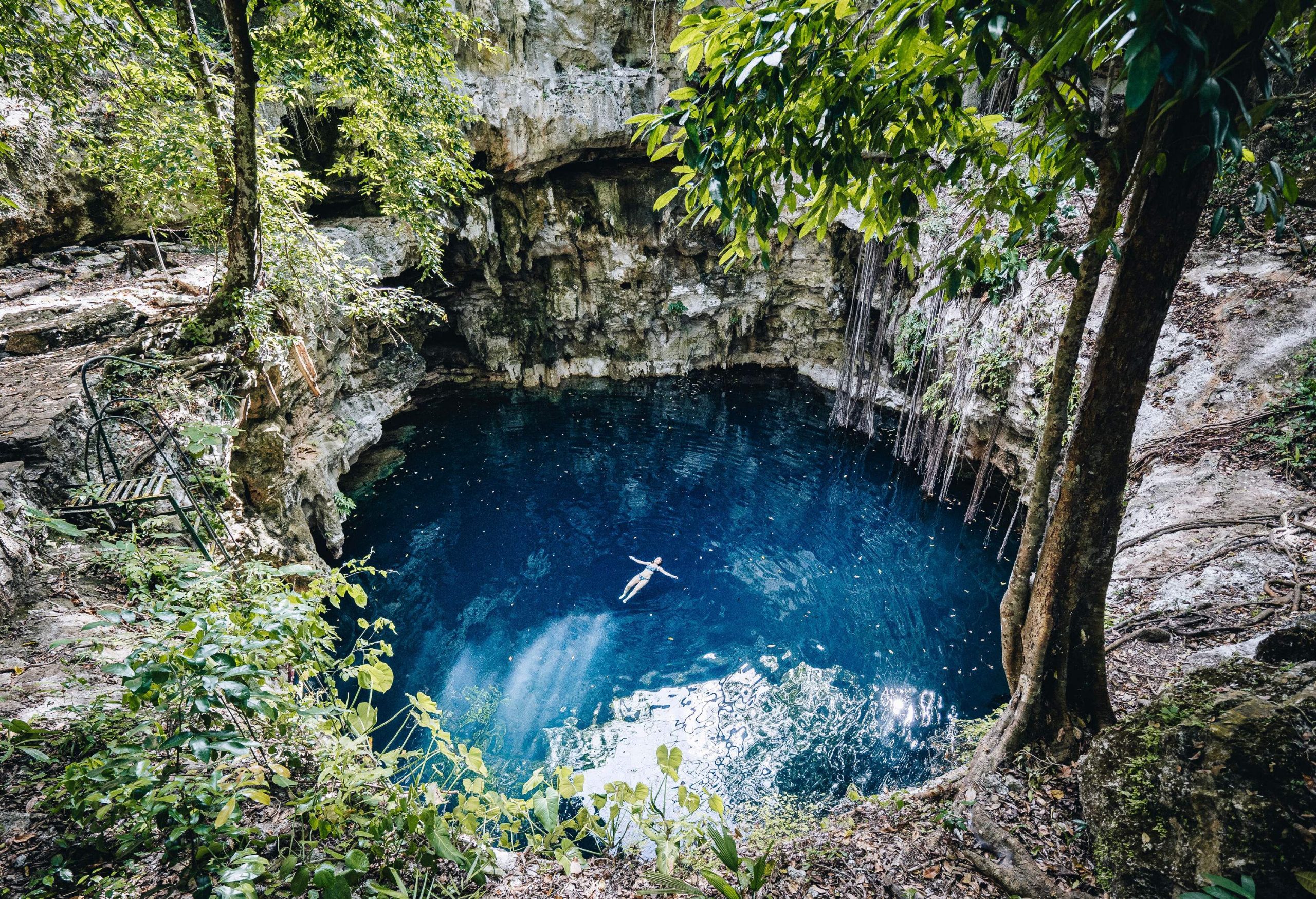 A woman floats on her back in the middle of a natural pit with clear waters.