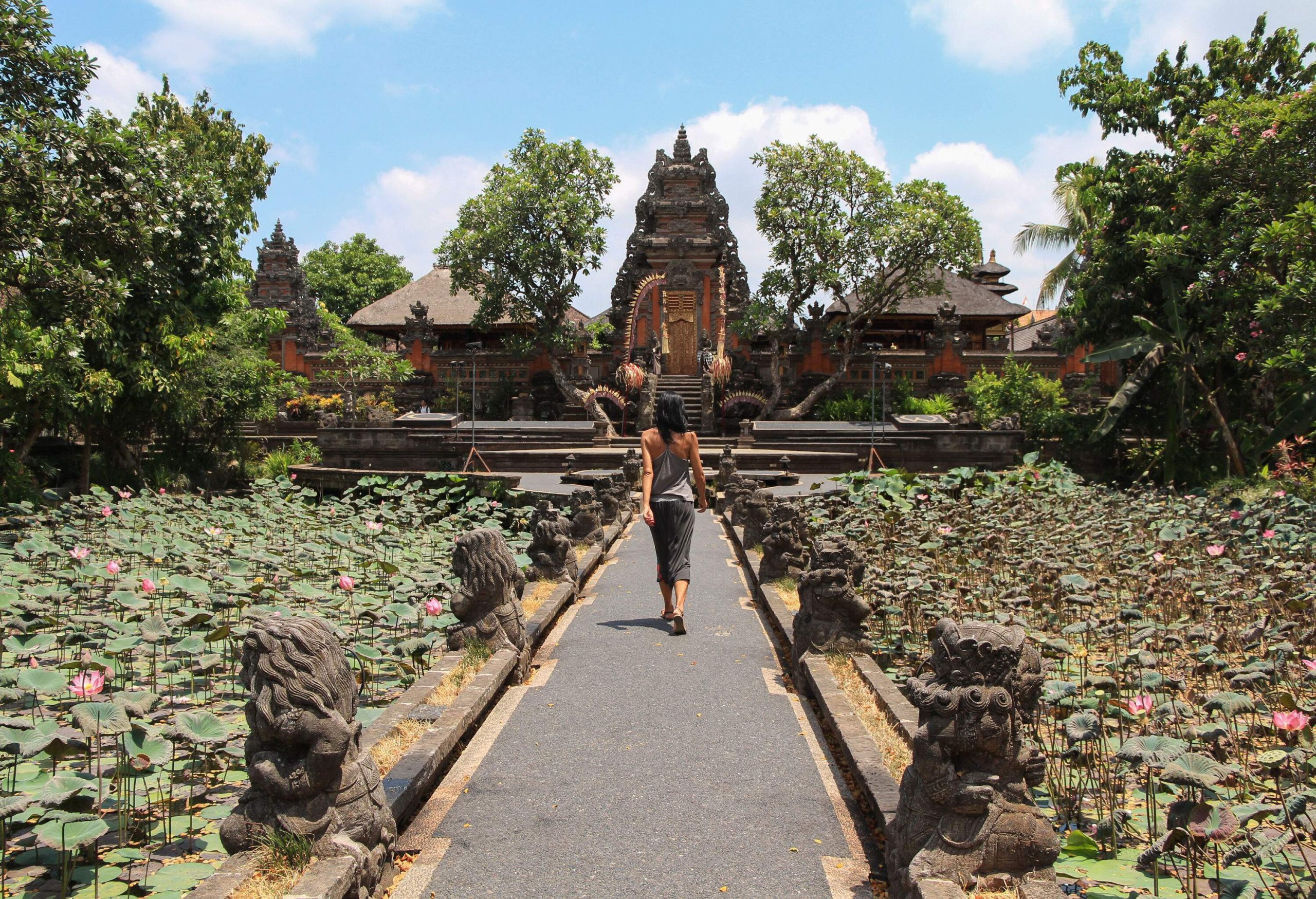A woman strolling in the direction of a temple down a pavement lined with statues.