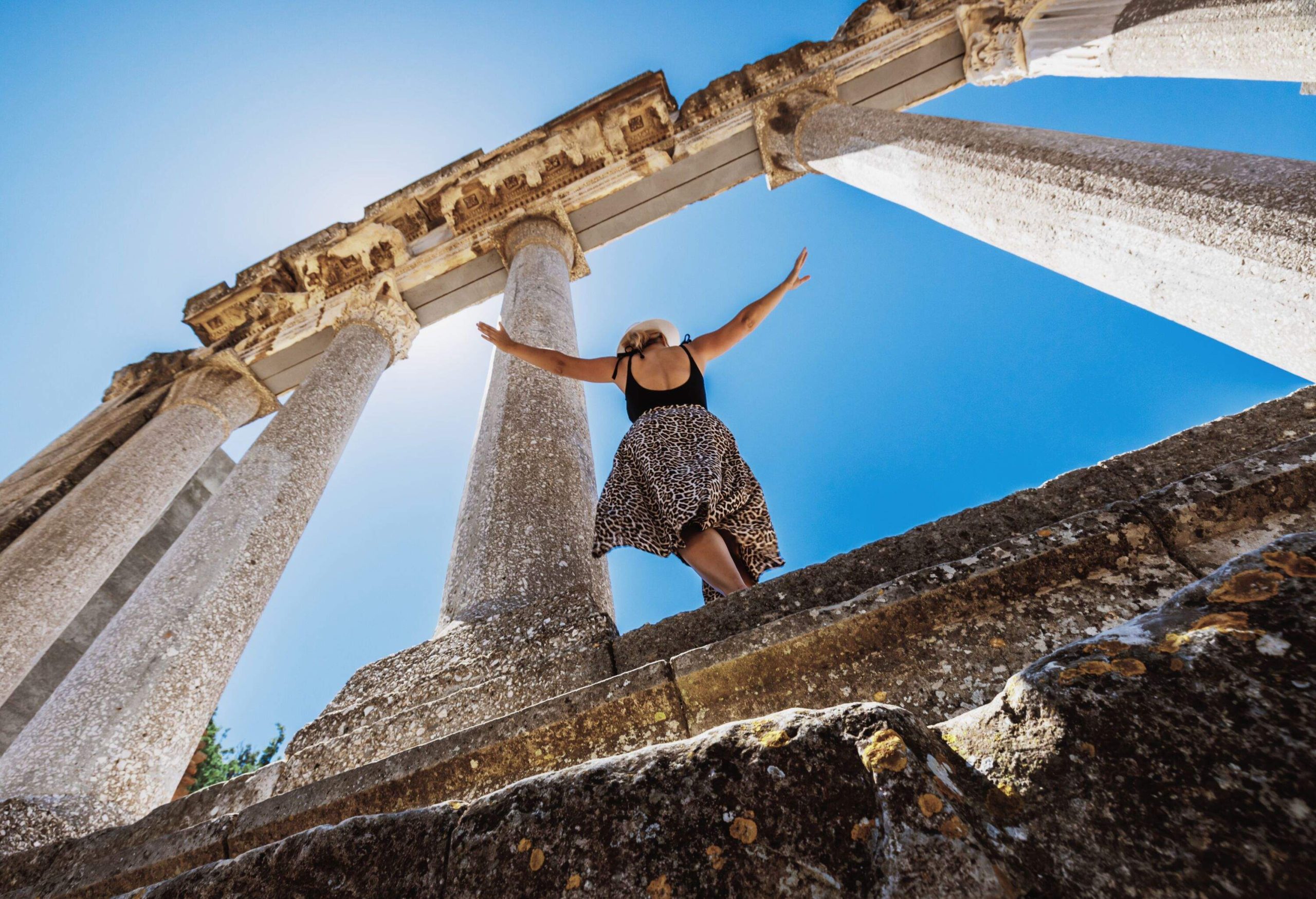 Woman enjoying with arms outstretched while exploring old historic monument against blue sky in summer