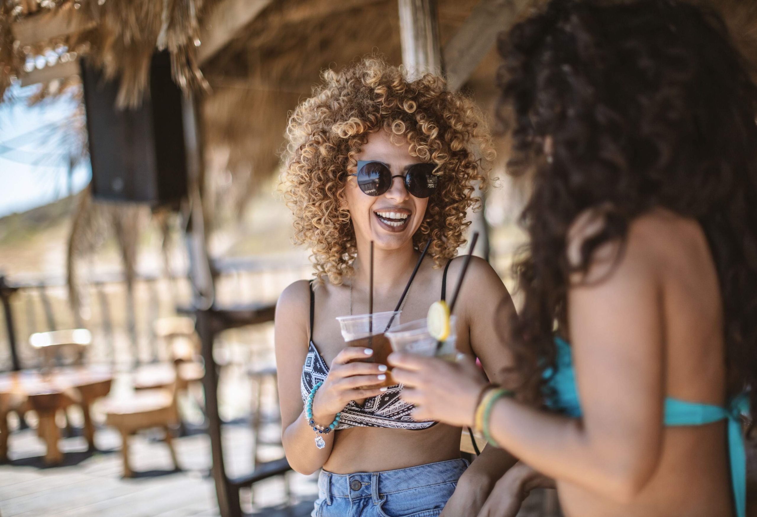 Two stunning girls in bathing suits enjoy themselves at a beach bar, with one of them sporting stylish sunglasses.