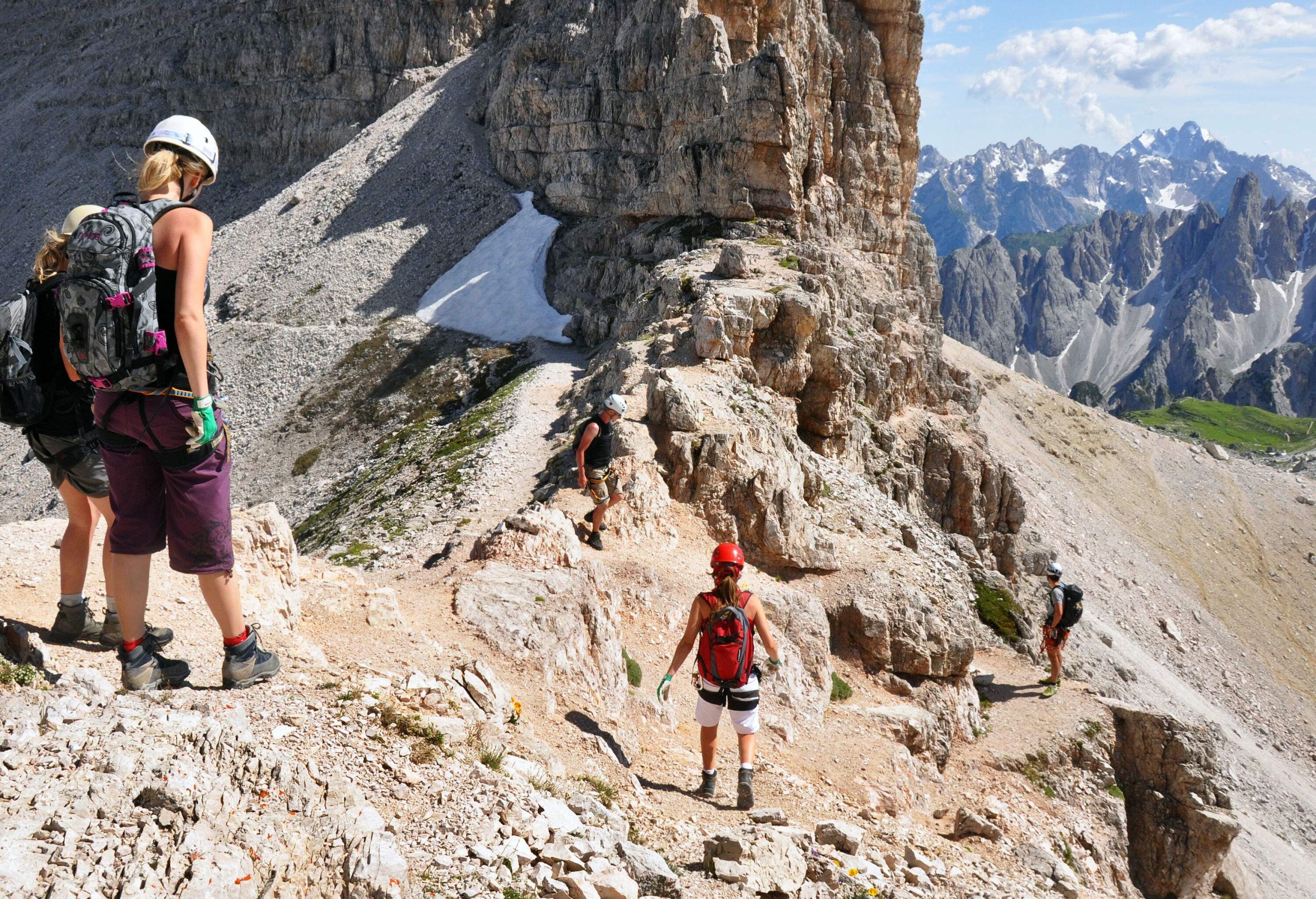 A group of people in helmets and backpacks are hiking on a steep mountain in the daytime.